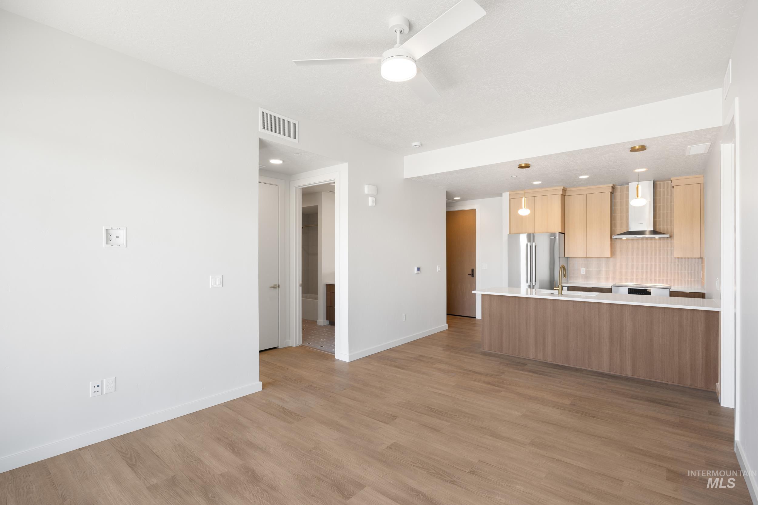 Kitchen featuring pendant lighting, wall chimney exhaust hood, decorative backsplash, open floor plan, and appliances with stainless steel finishes
