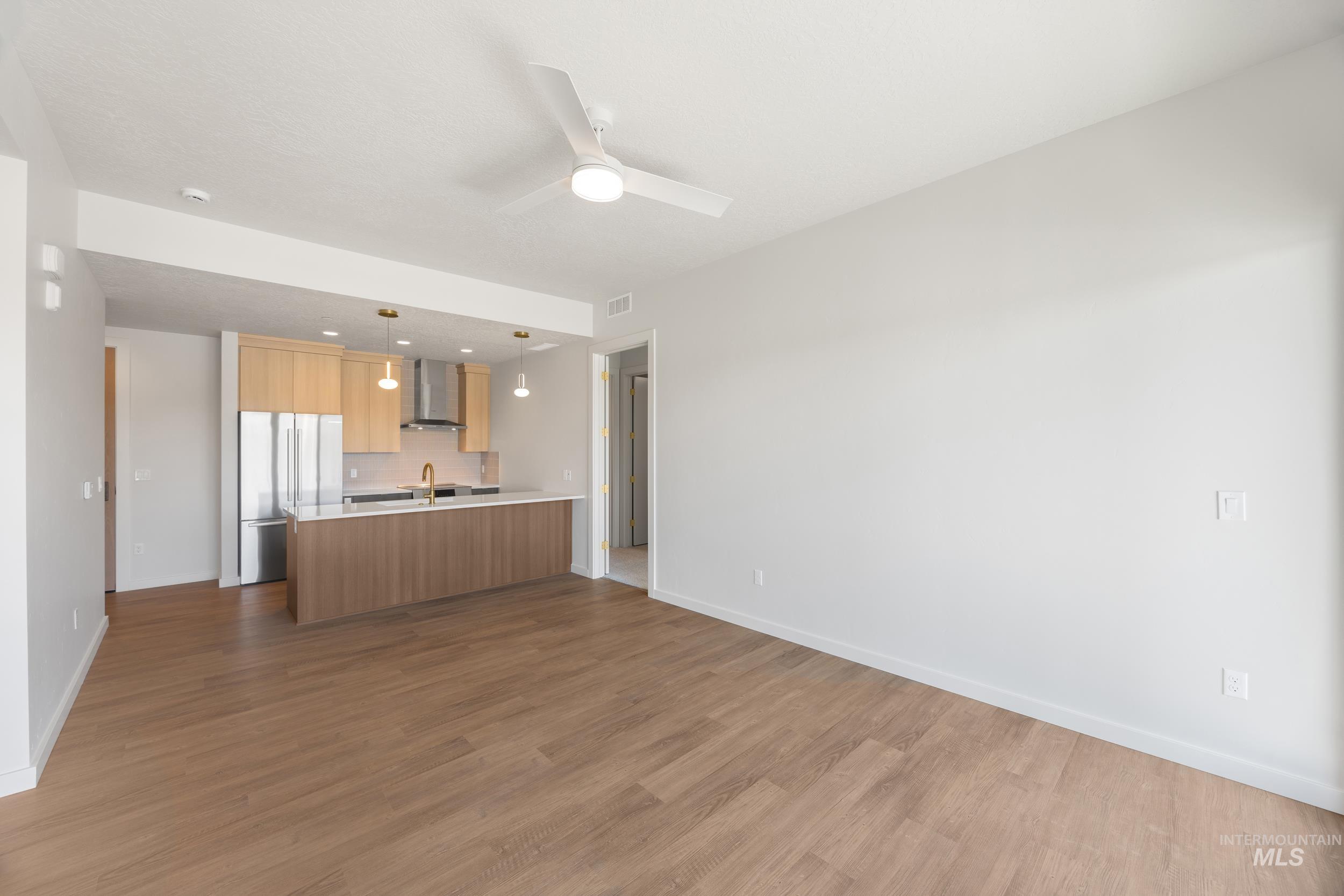 Kitchen with open floor plan, light countertops, stainless steel fridge, hanging light fixtures, and dark wood-type flooring