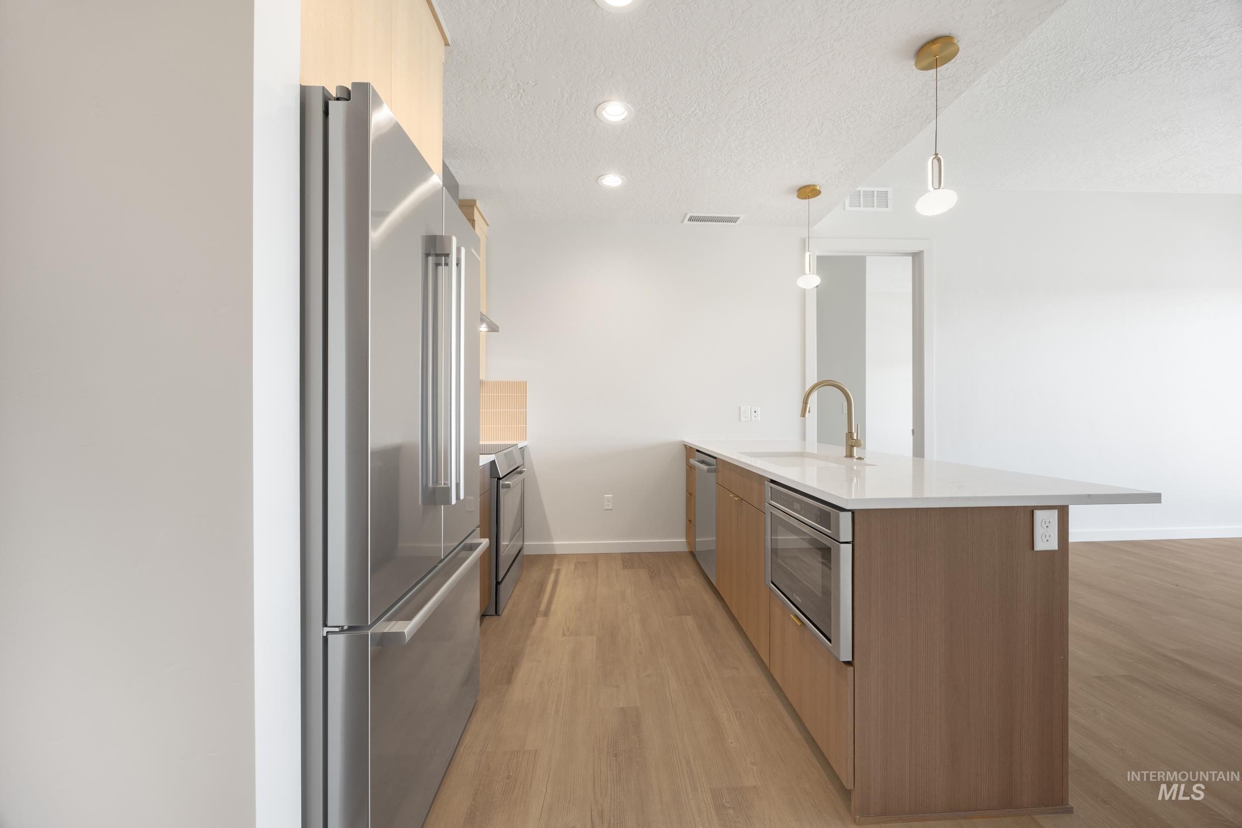Kitchen featuring modern cabinets, a peninsula, stainless steel appliances, a textured ceiling, and light stone counters