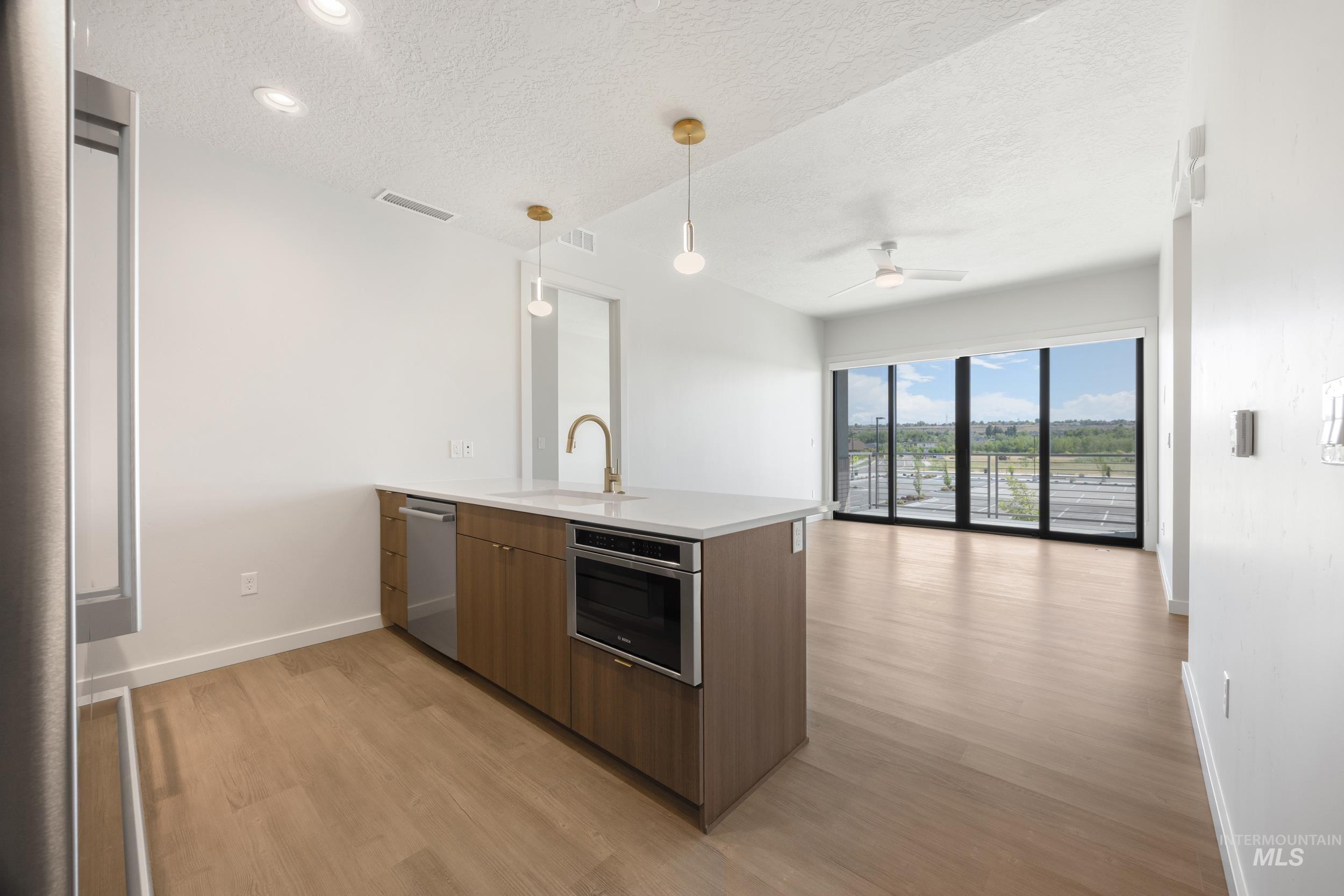 Kitchen with modern cabinets, hanging light fixtures, a textured ceiling, a peninsula, and light wood-style flooring