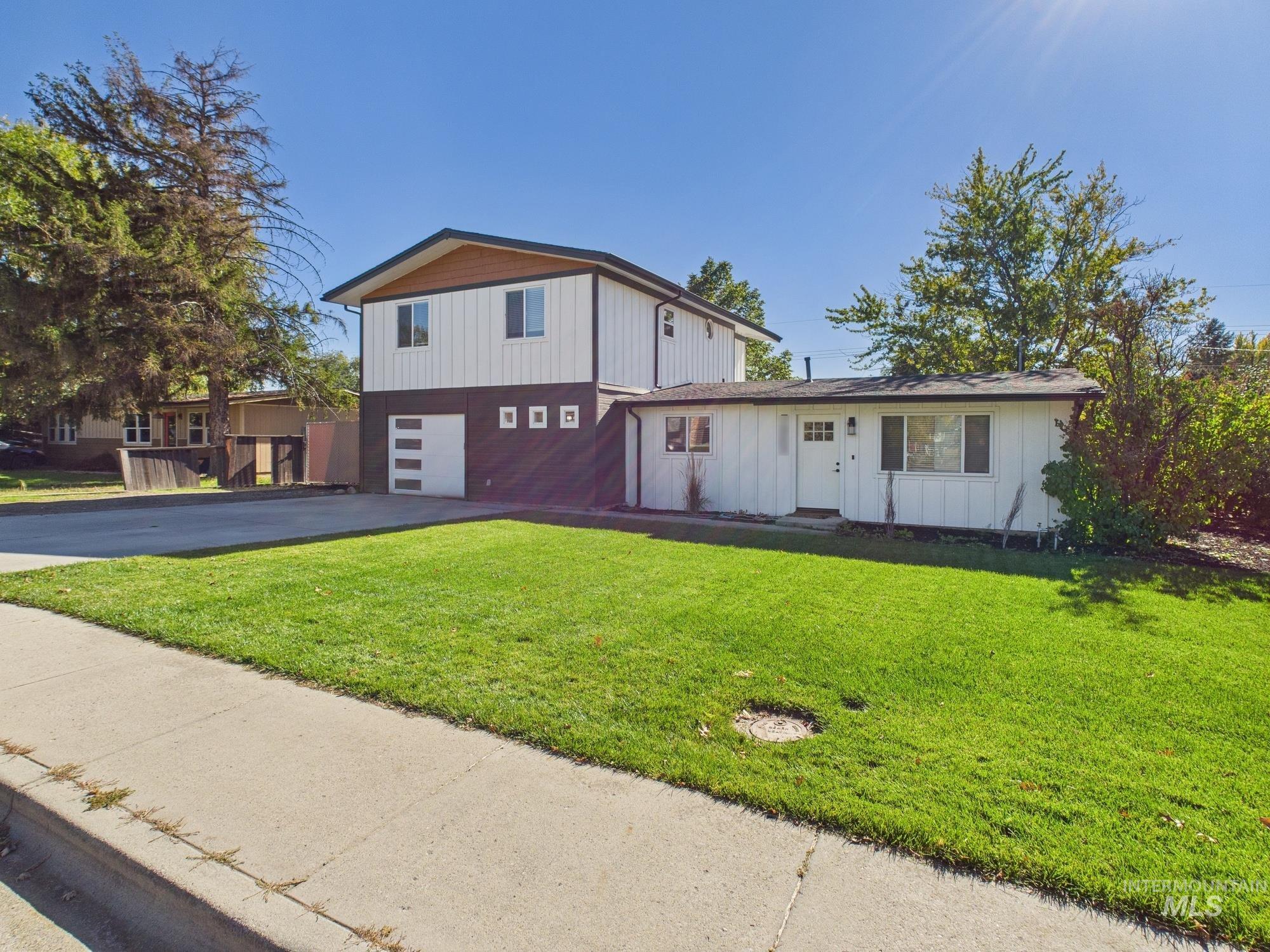 View of front facade featuring board and batten siding, a front lawn, driveway, and an attached garage