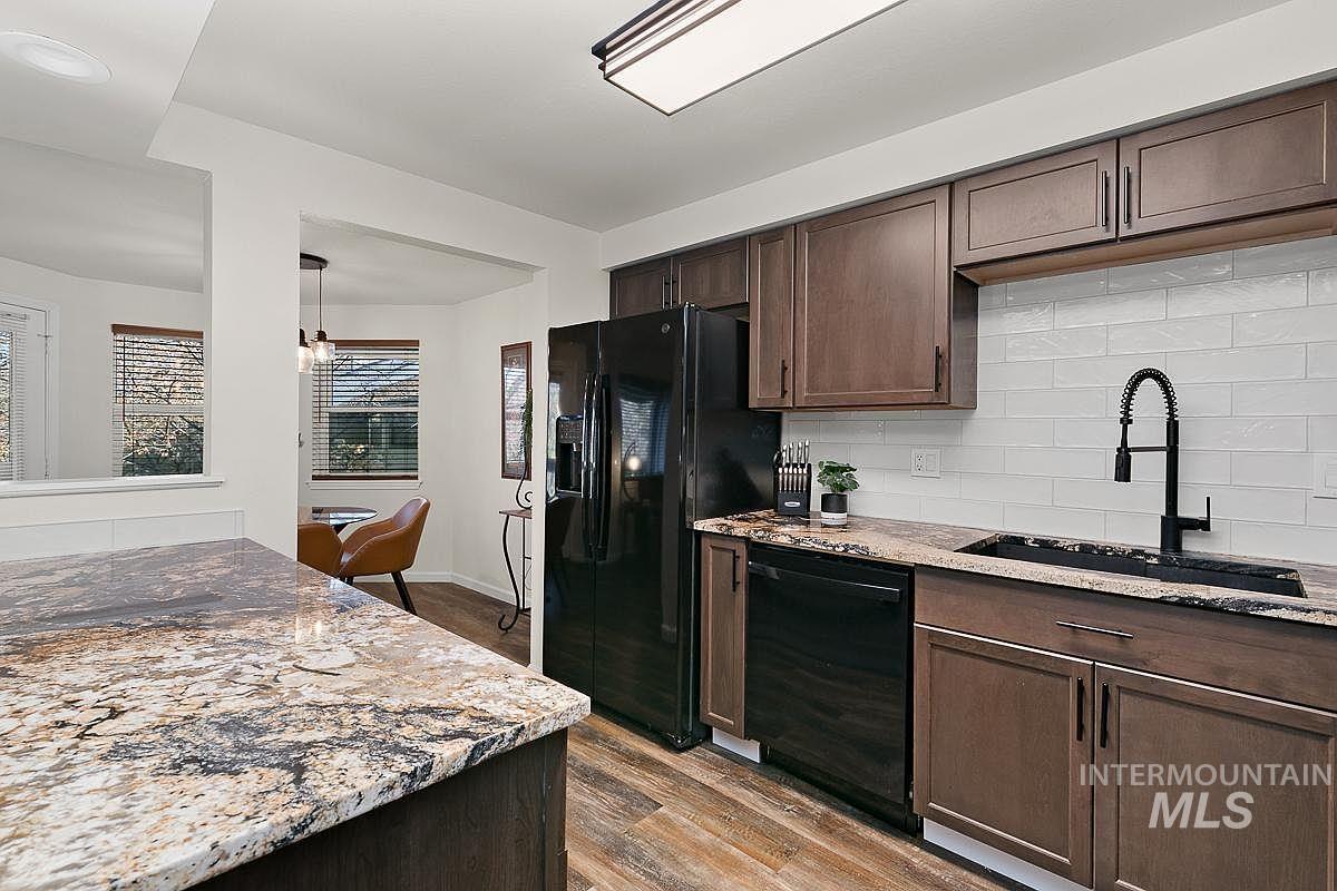 Kitchen featuring dark brown cabinets, tasteful backsplash, light stone counters, dark wood-type flooring, and black appliances