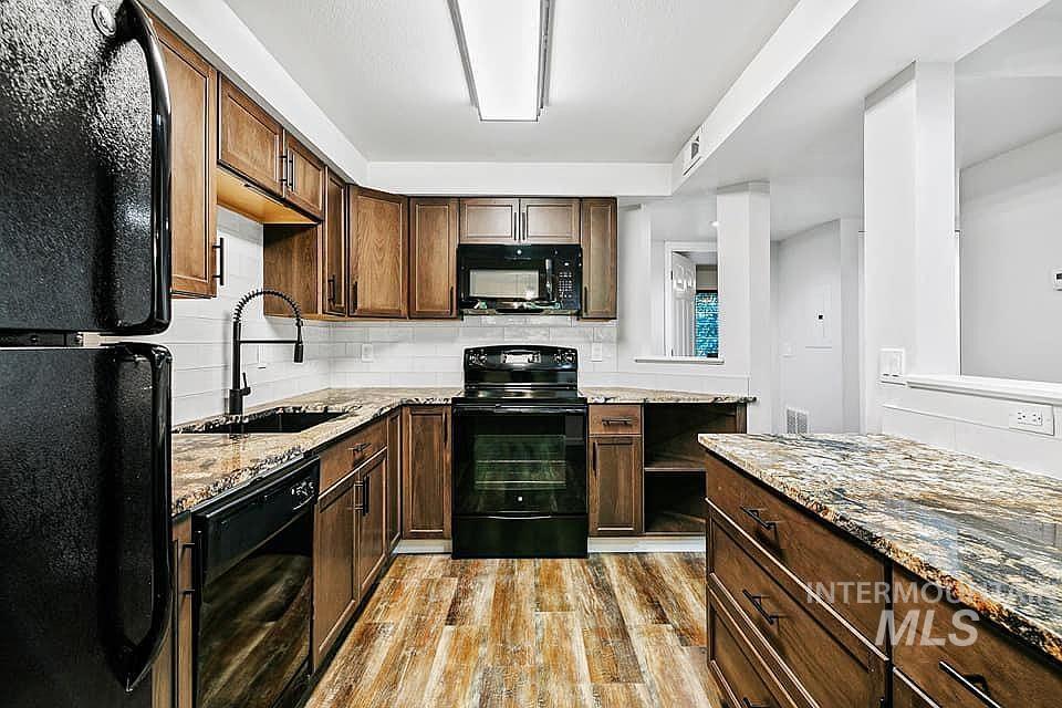 Kitchen with black appliances, dark brown cabinets, light wood-style floors, light stone countertops, and decorative backsplash