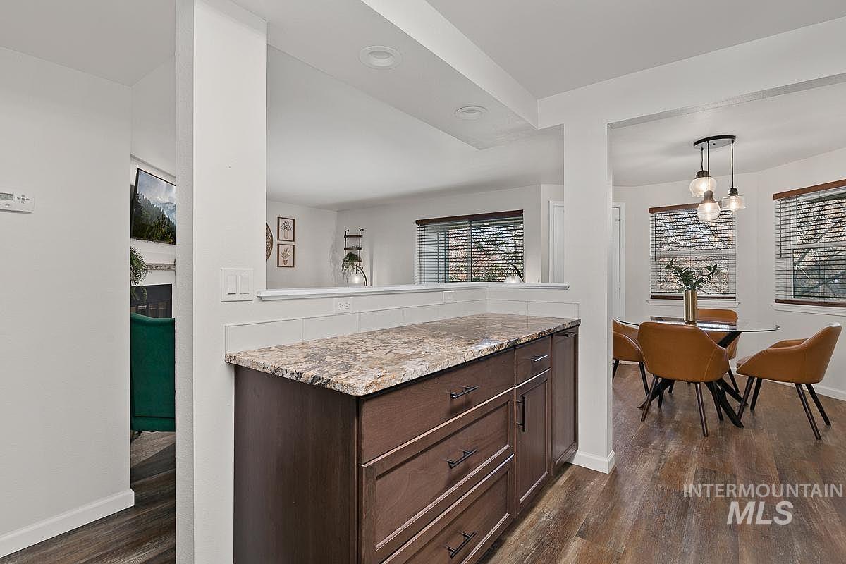 Kitchen with dark brown cabinets, light stone counters, dark wood-style floors, and hanging light fixtures