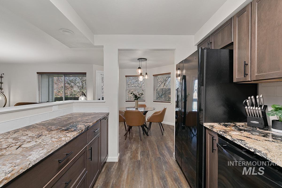 Kitchen with dark brown cabinets, light stone counters, black appliances, dark wood-style floors, and decorative light fixtures