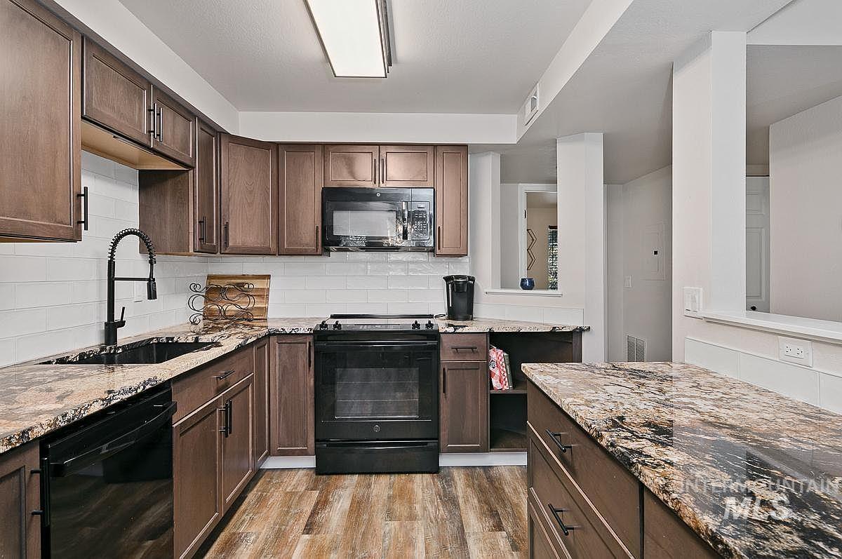 Kitchen featuring dark brown cabinets, black appliances, light stone counters, and light wood finished floors