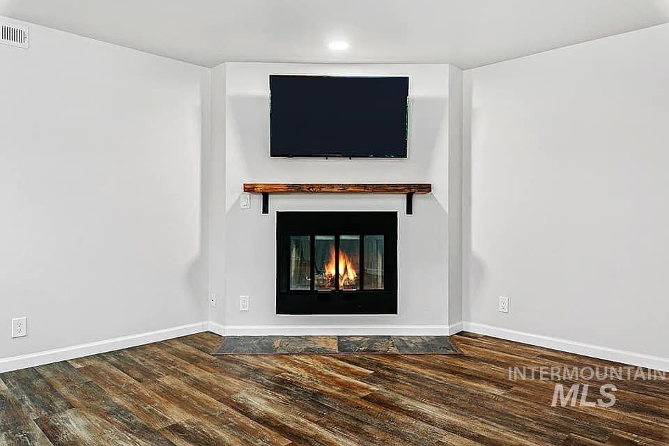 Unfurnished living room featuring a glass covered fireplace and dark wood-style floors