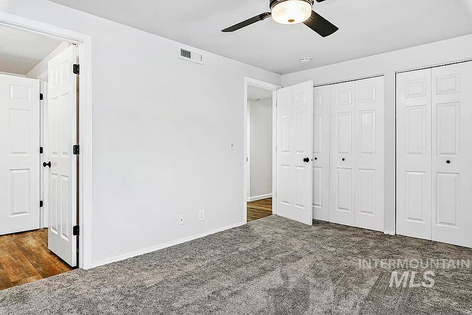 Unfurnished bedroom with multiple closets, dark colored carpet, and a ceiling fan