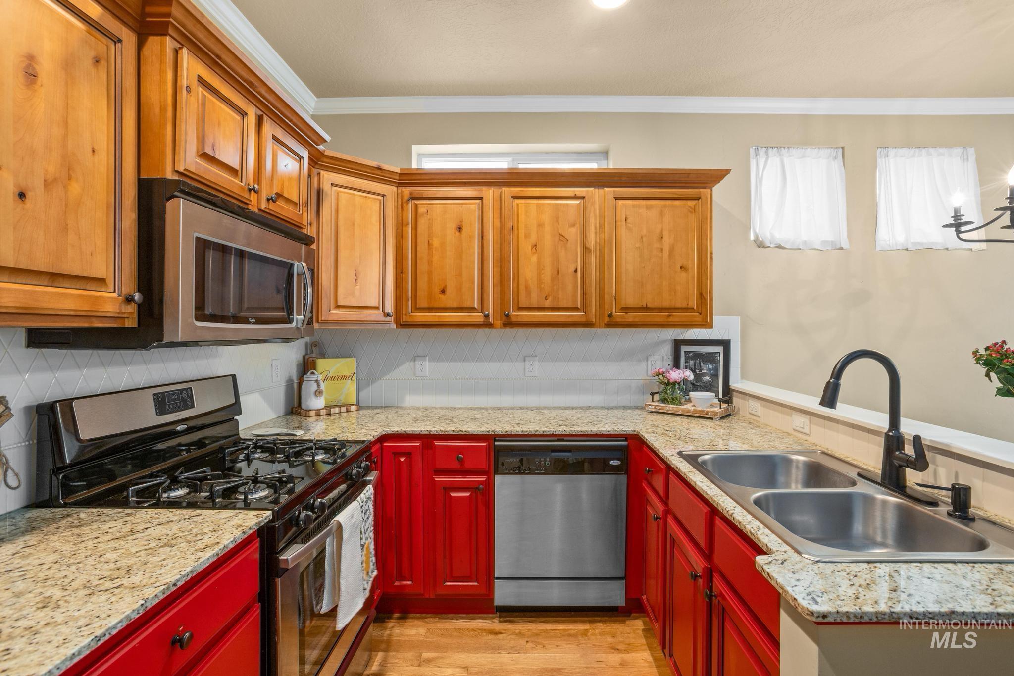 Kitchen featuring wood cabinetry, vibrant lower red cabinetry, granite-style countertops, and stainless steel appliances including a gas range, microwave, and dishwasher