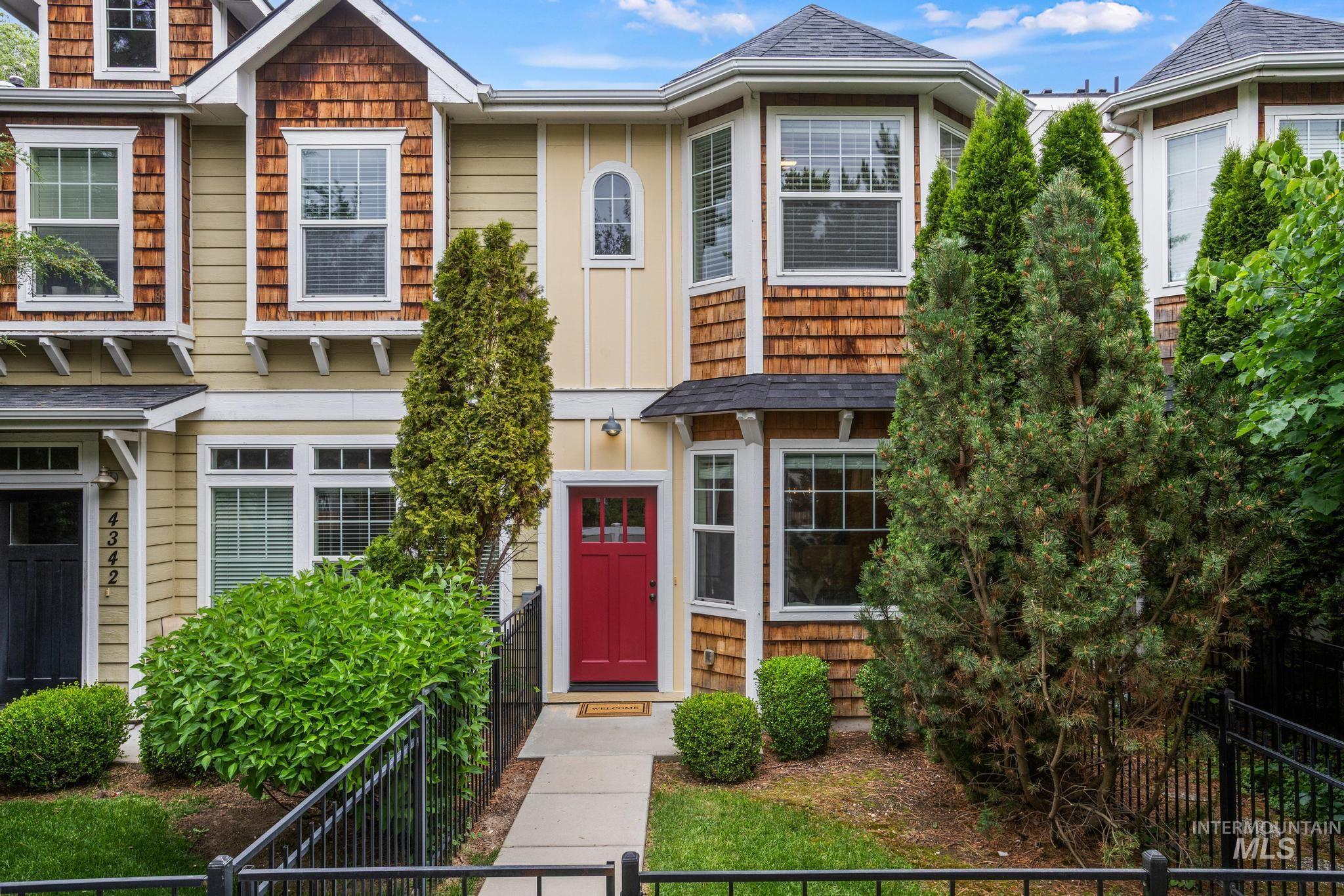 Multi-level townhome featuring a red entry door, bay window, natural wood shingles, and light yellow siding