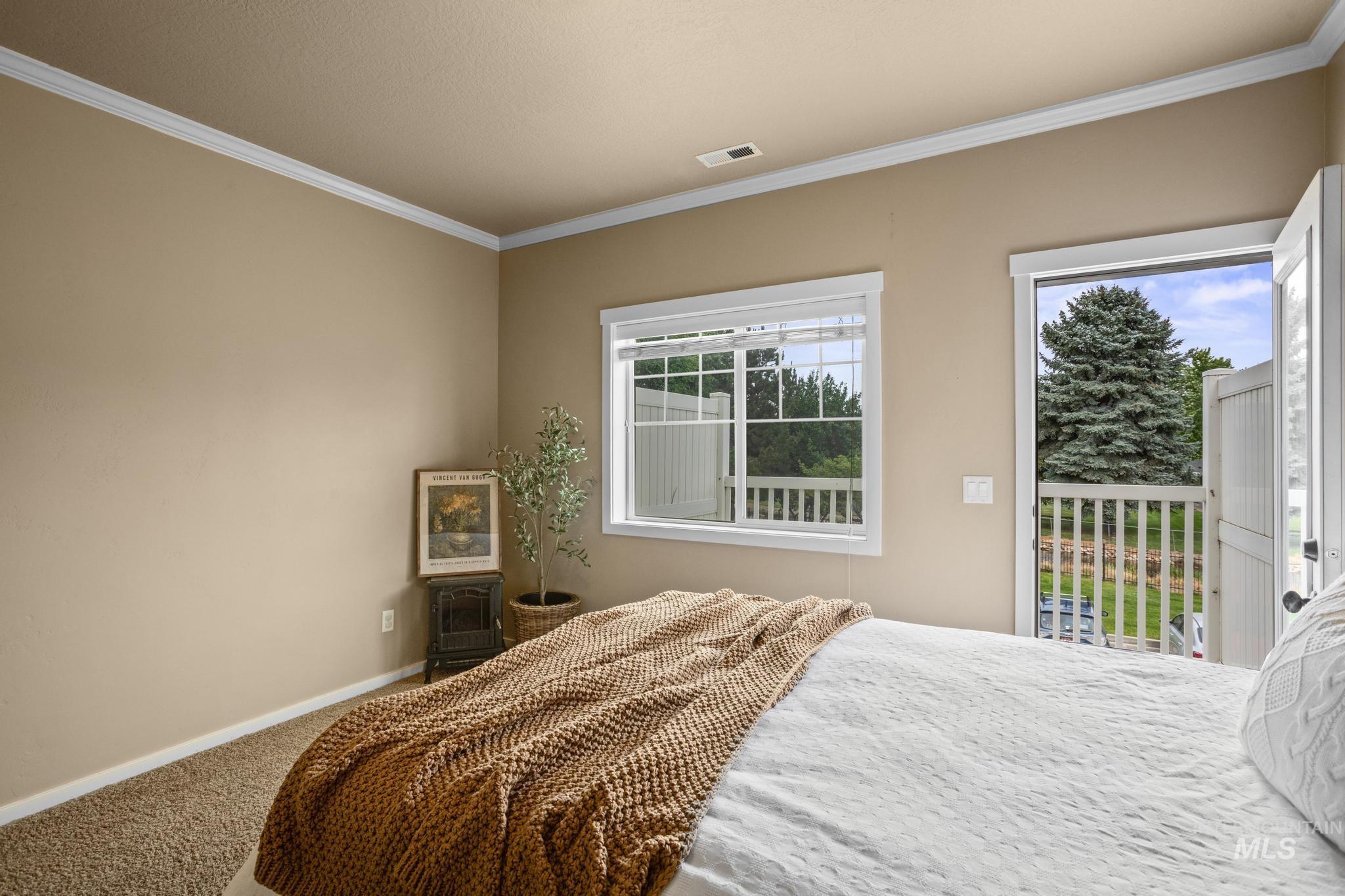 Bedroom featuring neutral wall color, white crown molding, carpeted flooring, a window, and a door opening to an outdoor balcony with white railings