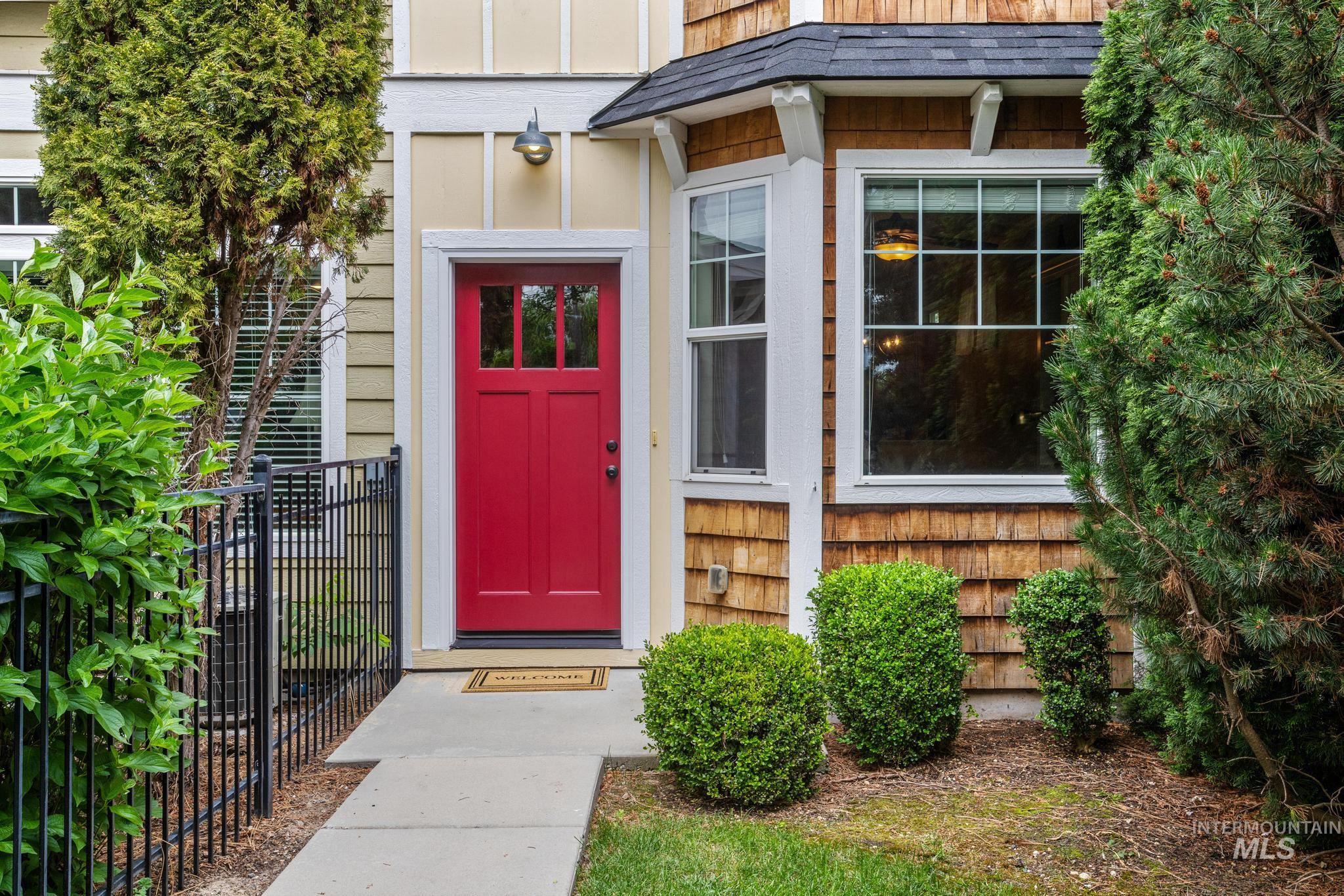Entryway featuring a bright red paneled door with glass inserts, a bay window with white trim, and natural wood shingle siding
