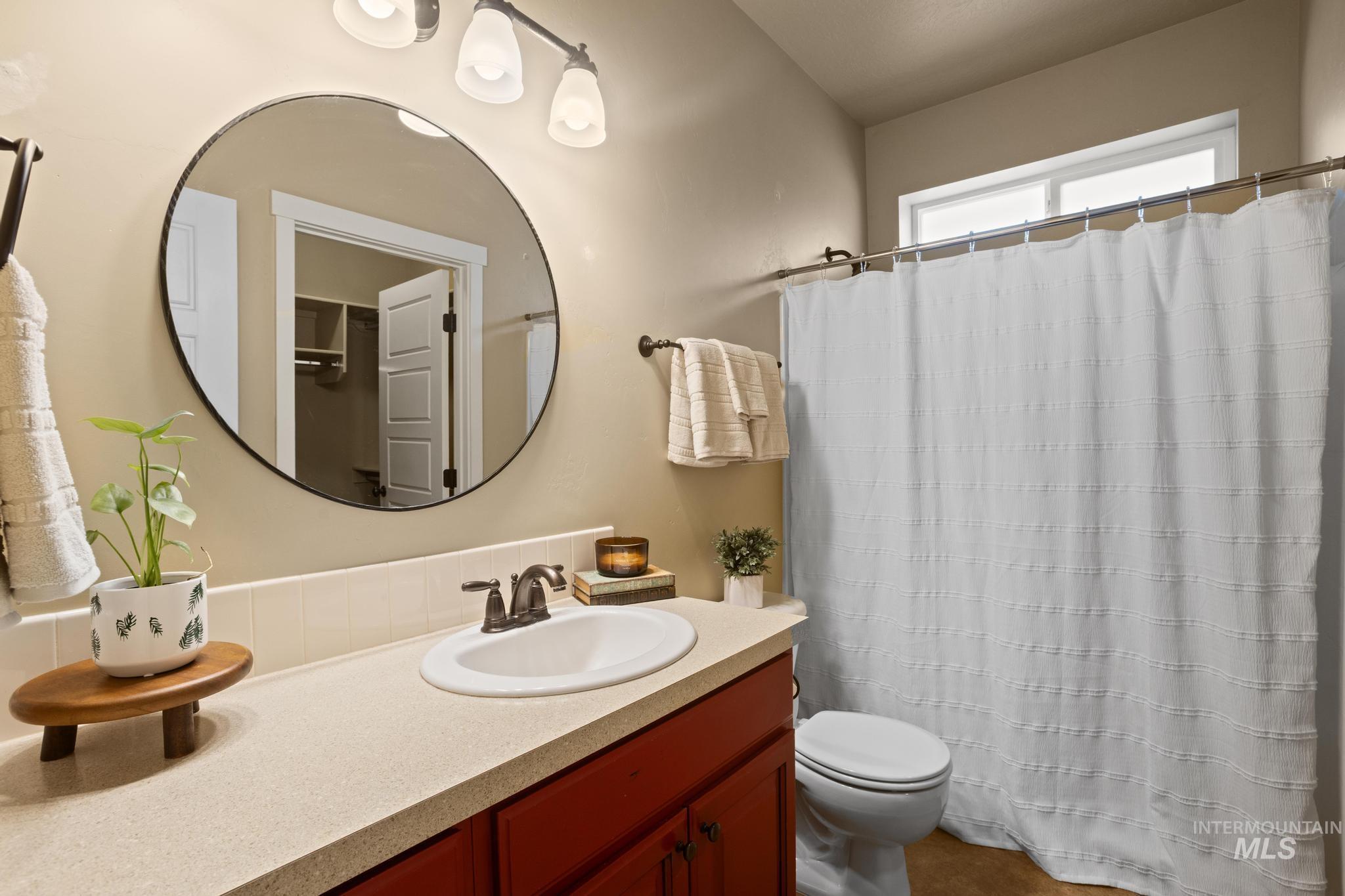 Bathroom vanity featuring a single basin sink with a bronze-finish faucet, a circular wall-mounted mirror, and a three-light vanity fixture