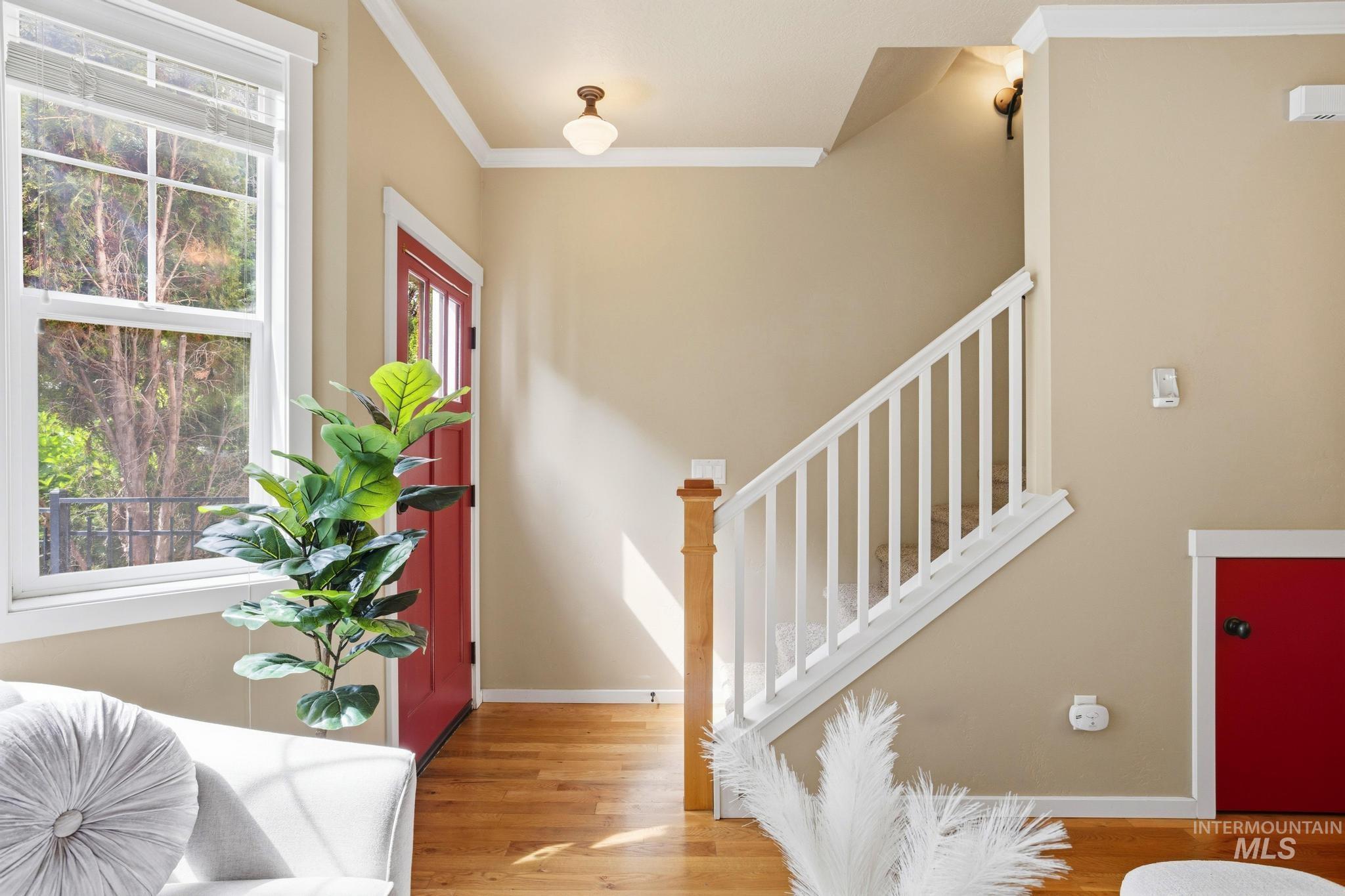 Entryway featuring wood-finish flooring, a red front door with integrated glass panes, and a white staircase with a natural wood newel post