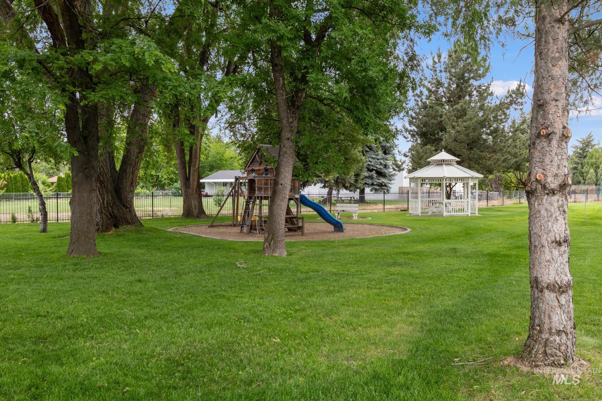 Expansive green space featuring mature trees, a wooden play structure, and a white gazebo