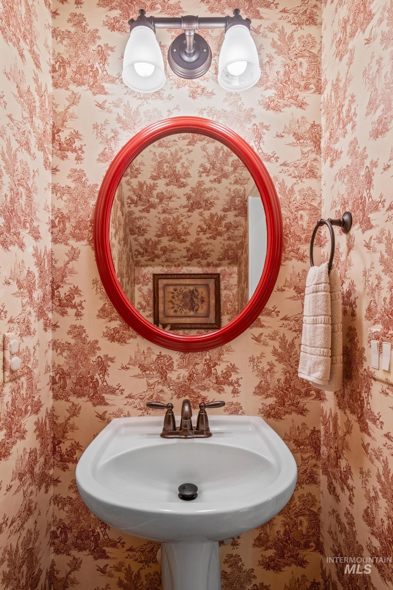 Pedestal sink with bronze-finish faucet, red oval mirror, and decorative wall-mounted light fixture