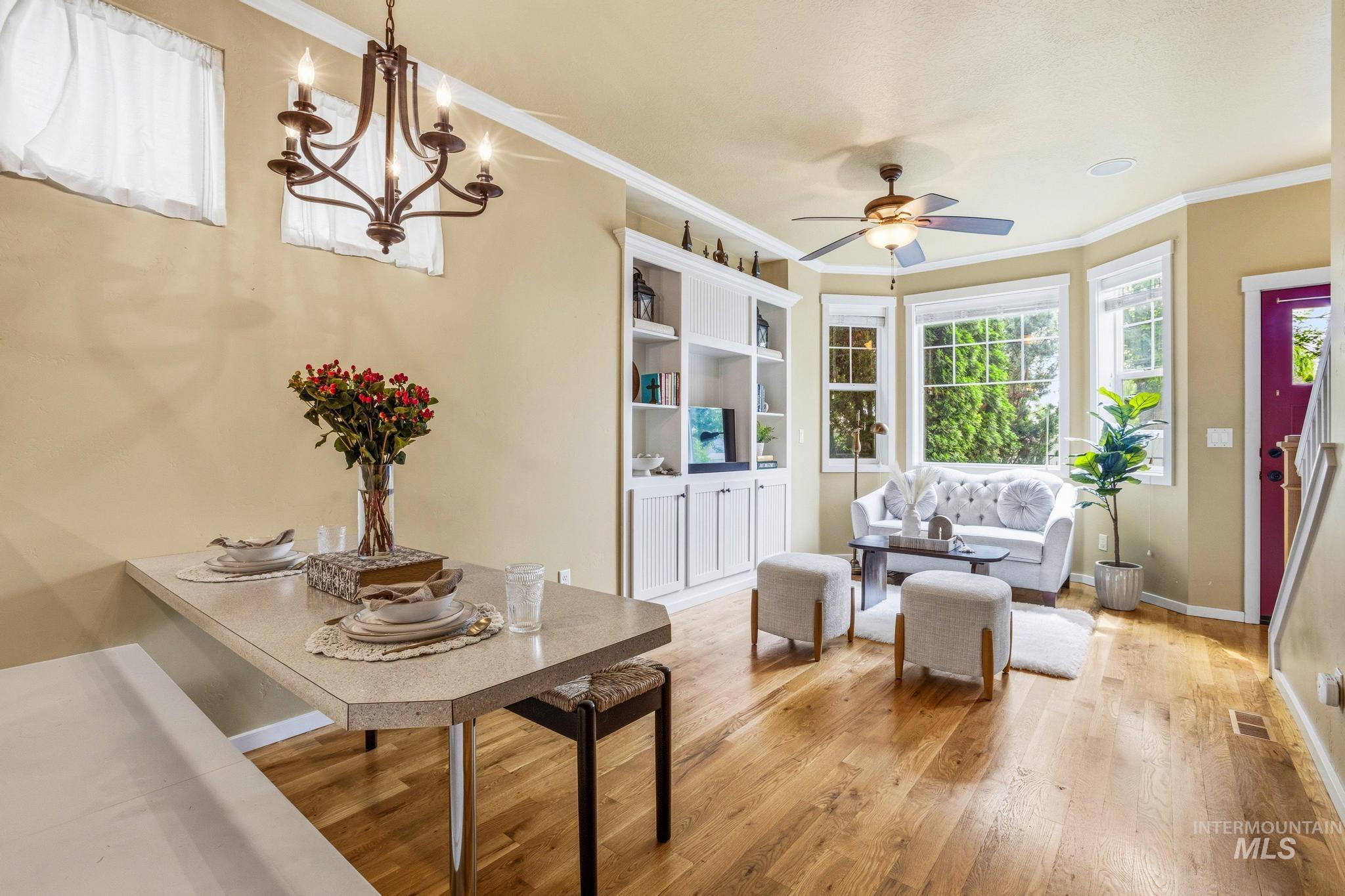 Open concept living area featuring wood-finish flooring, a built-in shelving unit, a bay window, a ceiling fan, and an integrated dining nook with a wall-mounted countertop