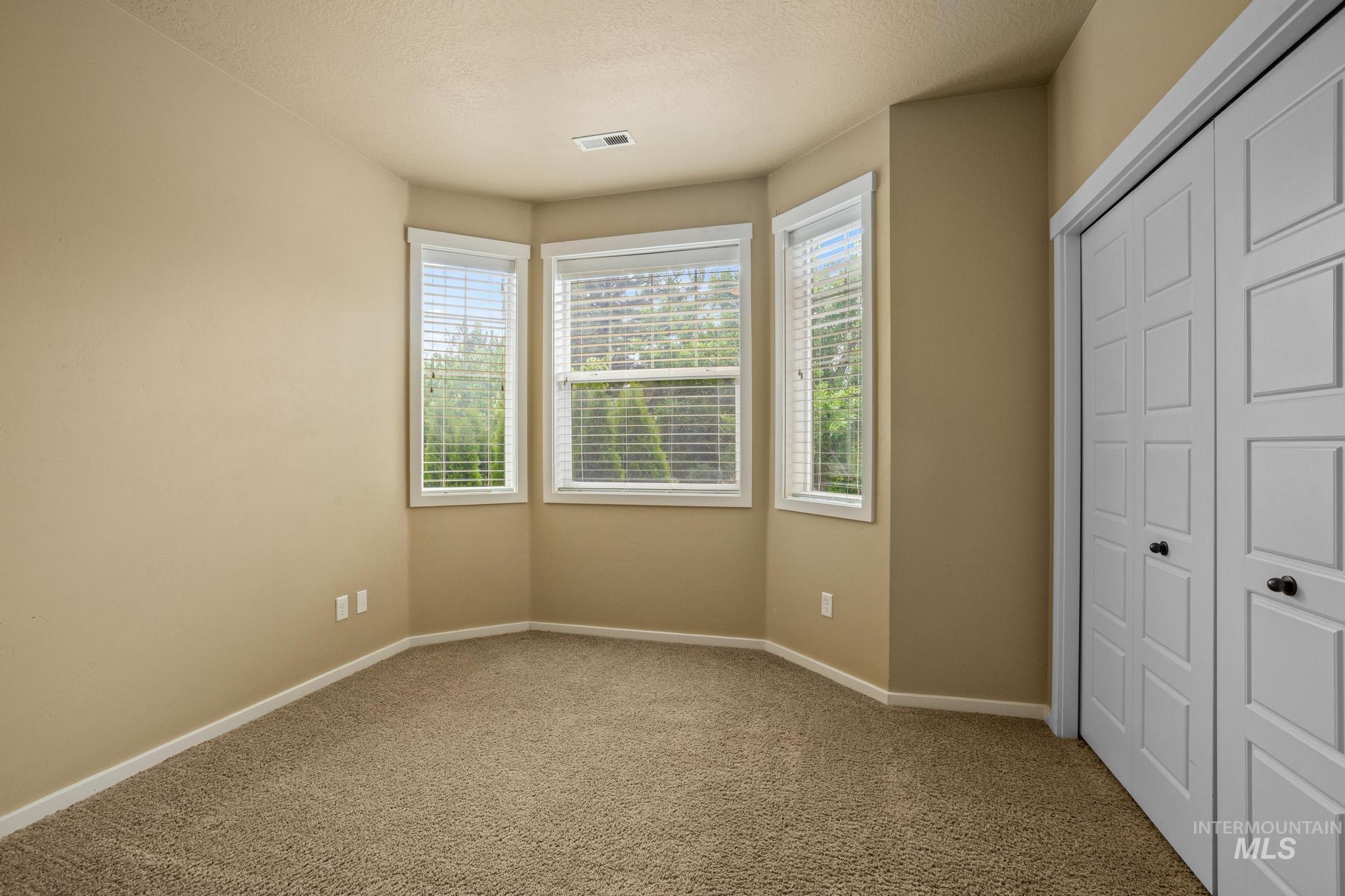 Bay window with three individual pane windows, neutral carpeting, light-toned wall paint, and bi-fold closet doors with black hardware