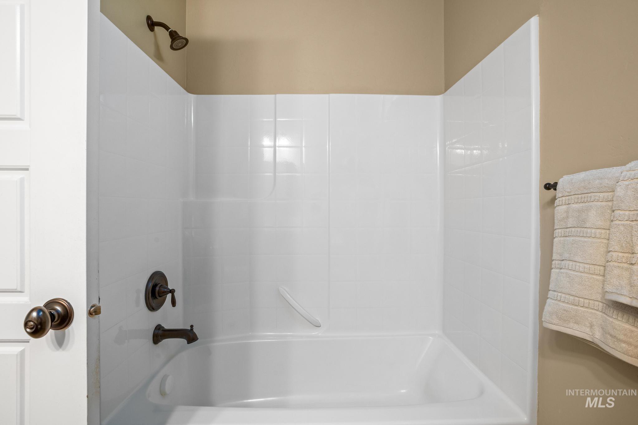 White bathtub and shower combination featuring dark bronze fixtures