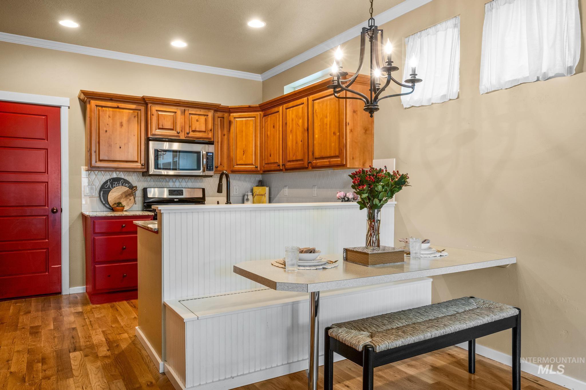 Kitchen area featuring wood-finish flooring, wood cabinetry, stainless steel appliances, a tile backsplash, and a built-in banquette with a white beadboard finish