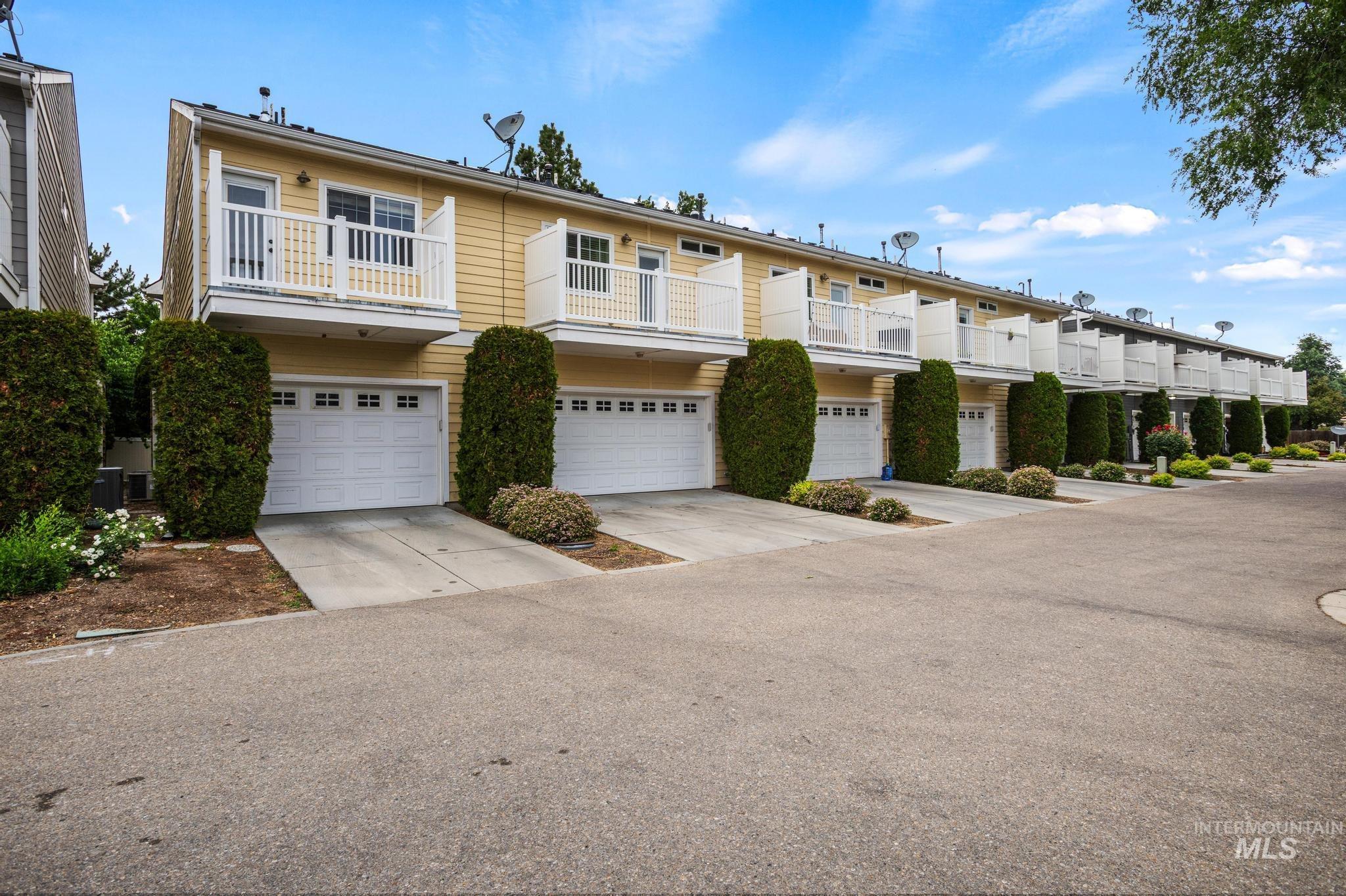 Row of townhomes featuring individual garages, private balconies with white railings, and yellow siding
