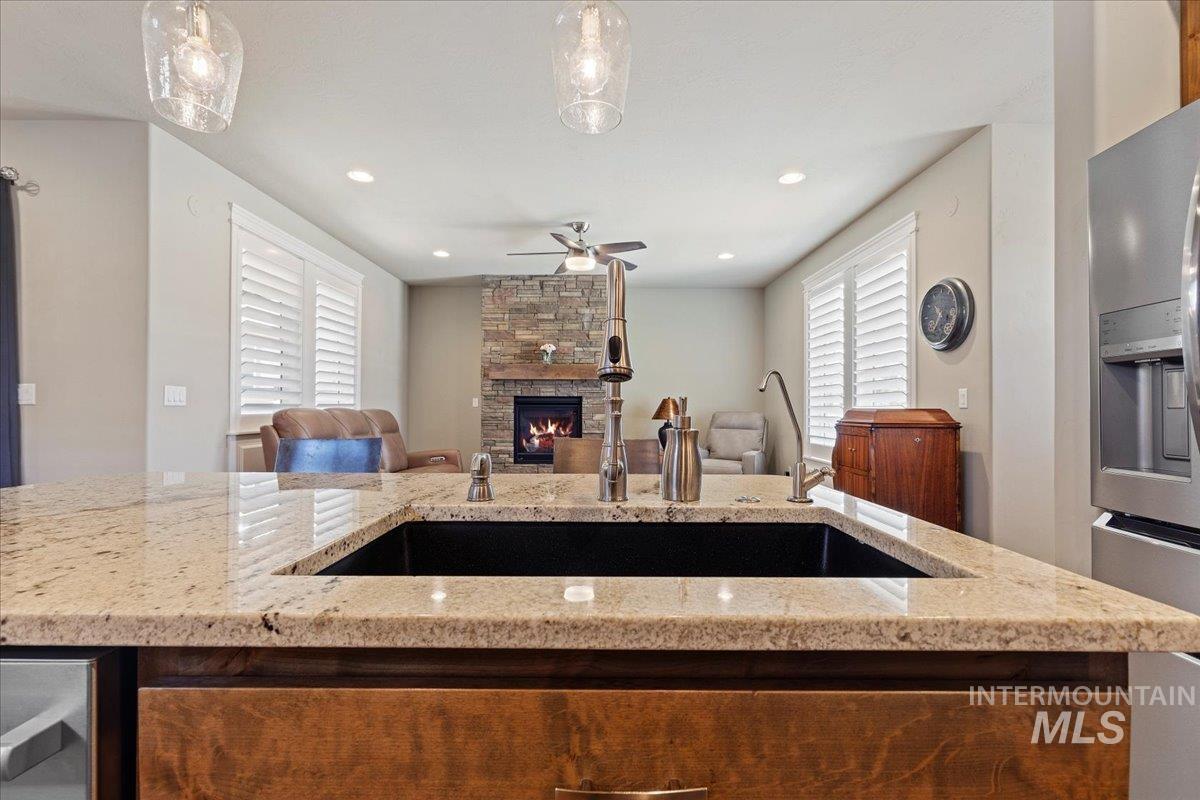 Kitchen featuring open floor plan, ceiling fan, a stone fireplace, light stone counters, and recessed lighting