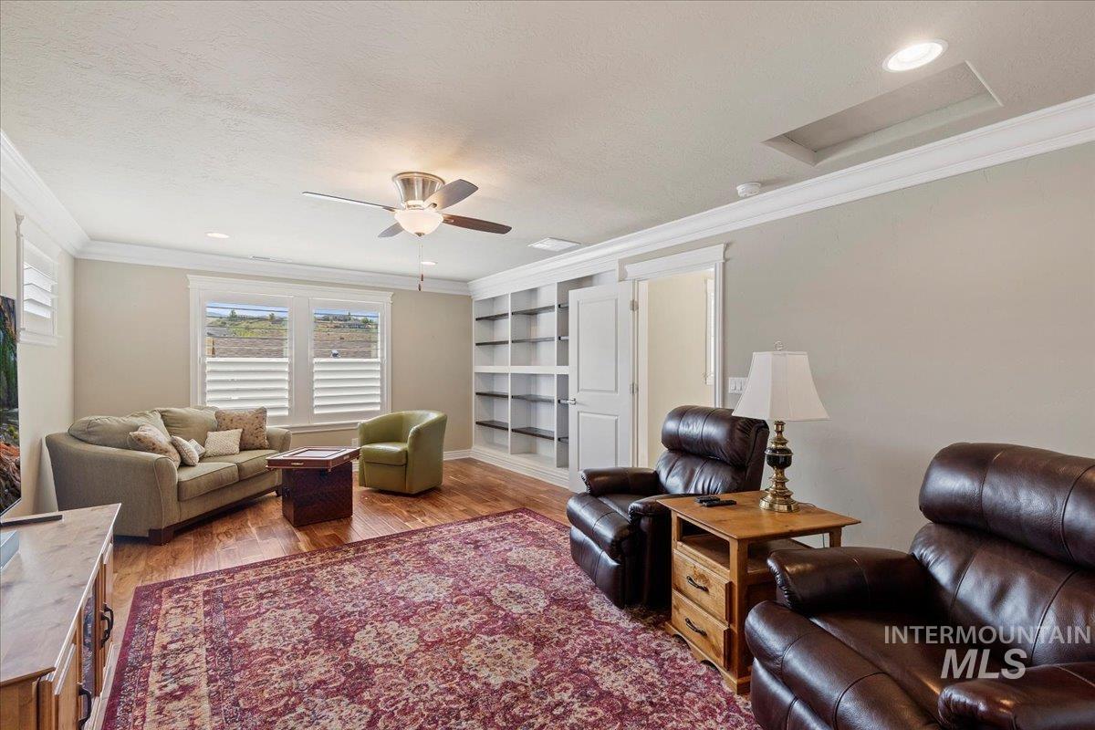 Living room with attic access, crown molding, a ceiling fan, and light wood finished floors