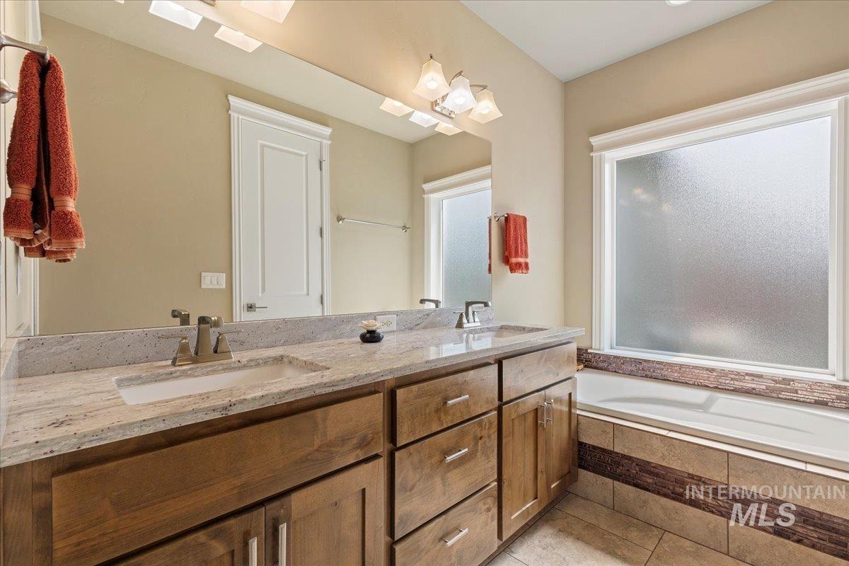 Full bathroom featuring double vanity, tiled bath, plenty of natural light, and tile patterned flooring