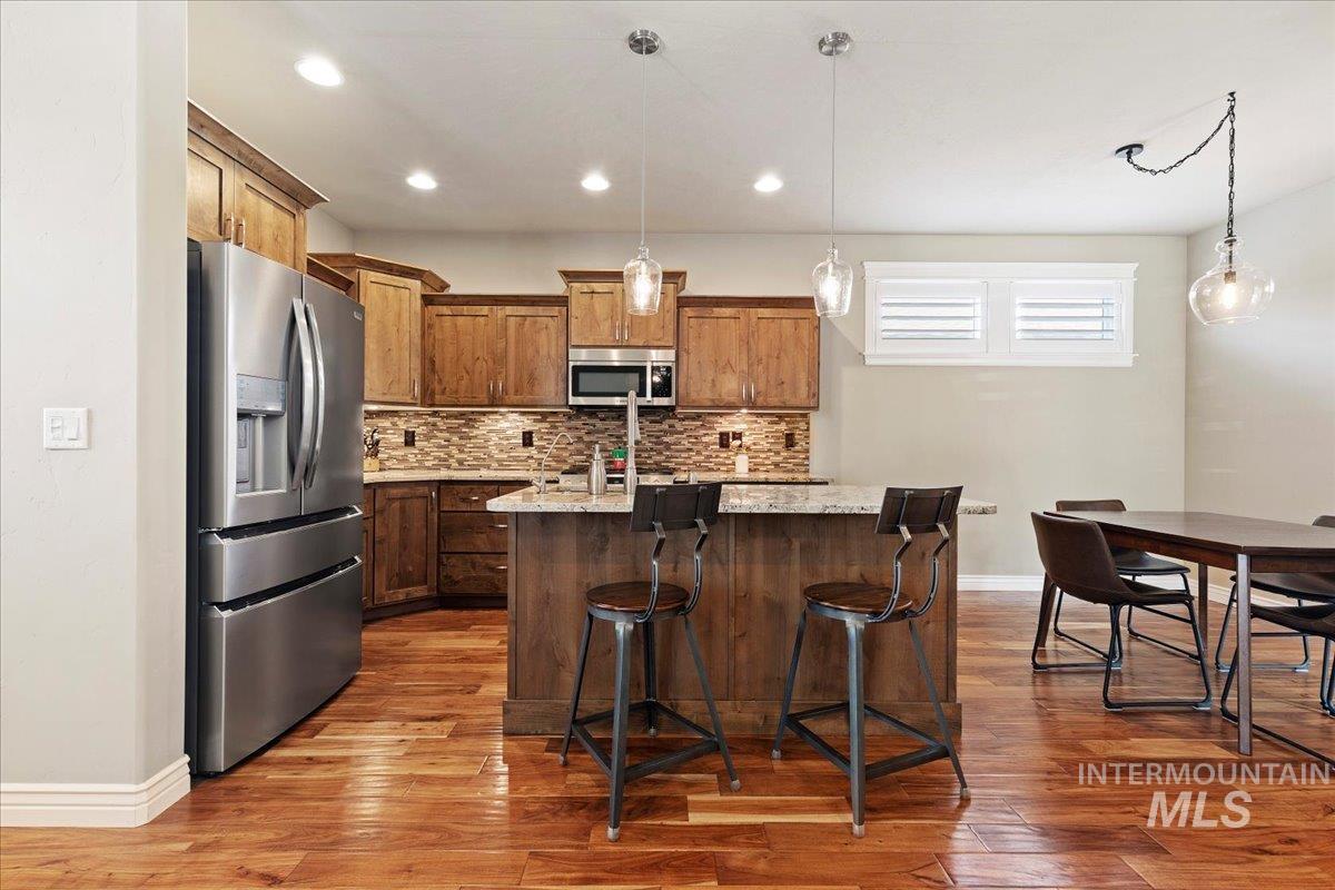 Kitchen featuring stainless steel appliances, dark wood-style flooring, tasteful backsplash, a center island with sink, and hanging light fixtures