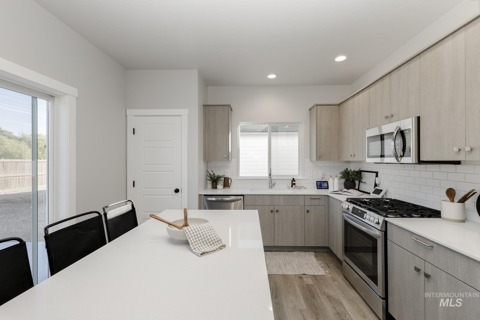 Kitchen featuring appliances with stainless steel finishes, decorative backsplash, light brown cabinets, light wood-type flooring, and modern cabinets