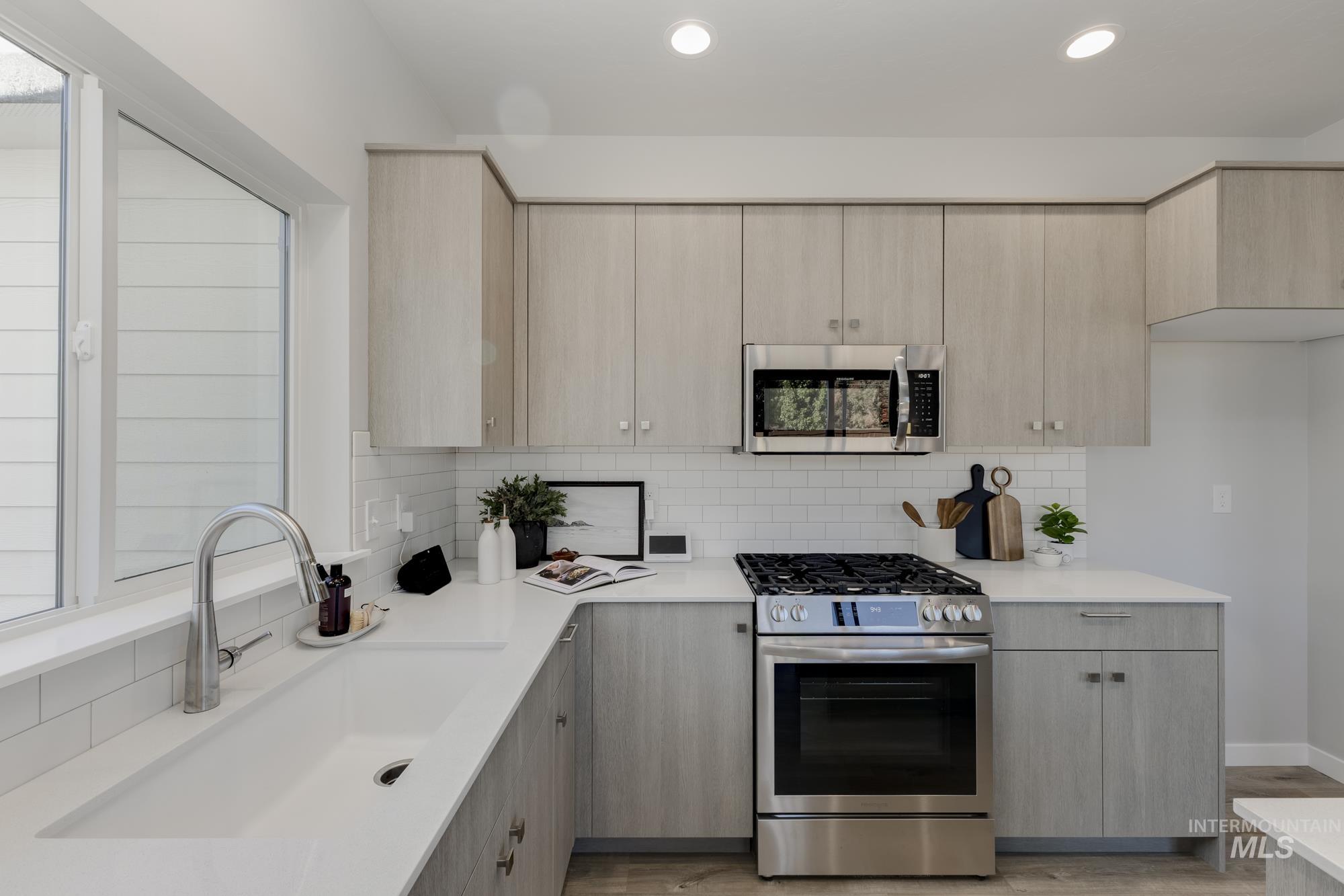Kitchen featuring light brown cabinetry, appliances with stainless steel finishes, decorative backsplash, light wood-type flooring, and modern cabinets