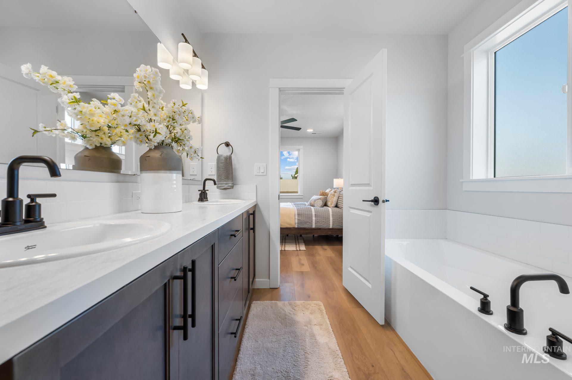 Ensuite bathroom with double vanity, light wood-style floors, a bath, and a ceiling fan
