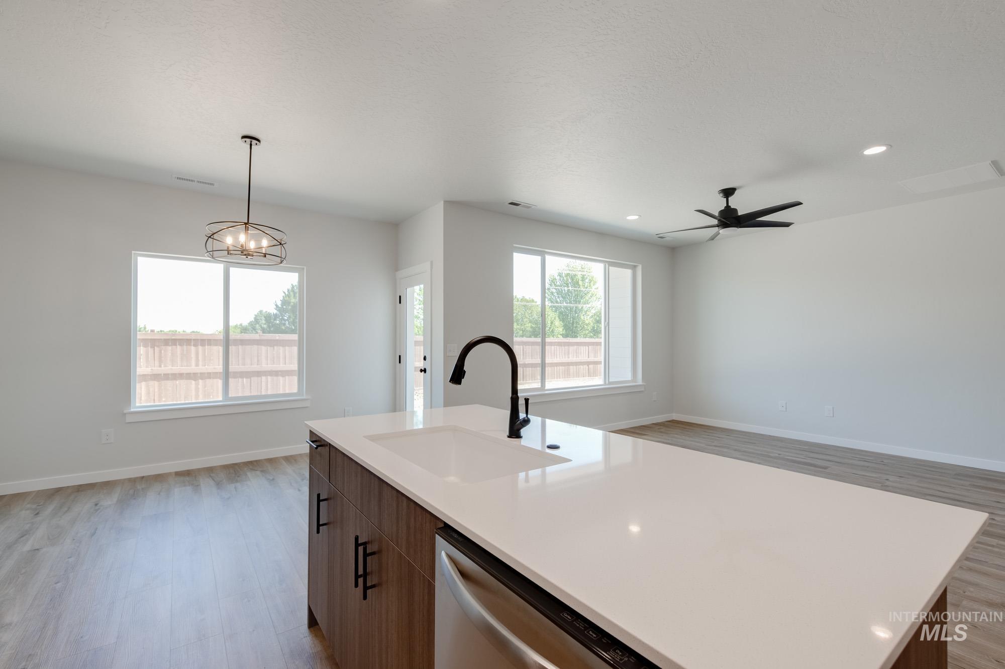 Kitchen featuring open floor plan, stainless steel dishwasher, light wood-style floors, light countertops, and a center island with sink