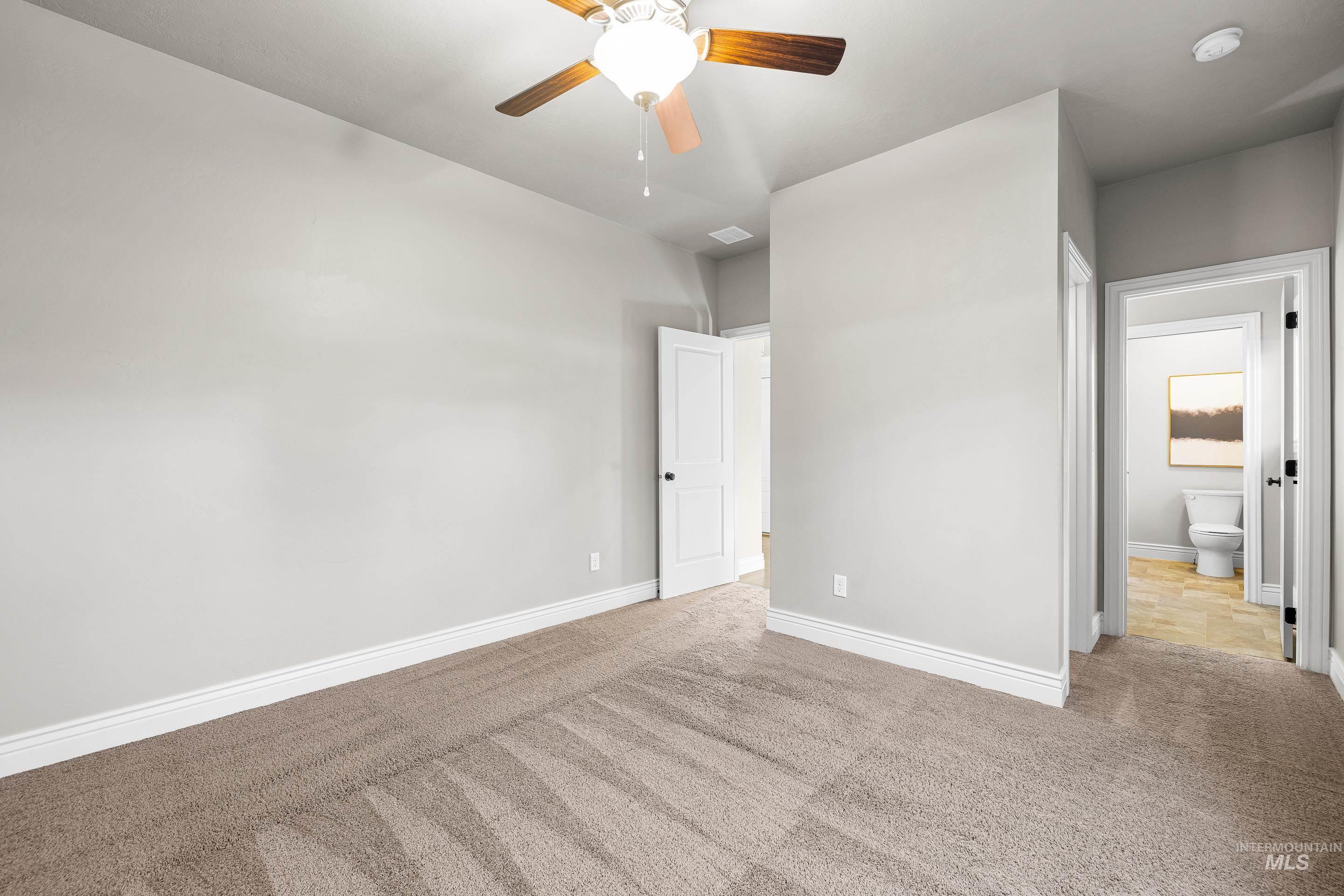Unfurnished bedroom featuring carpet, ensuite bathroom, and ceiling fan