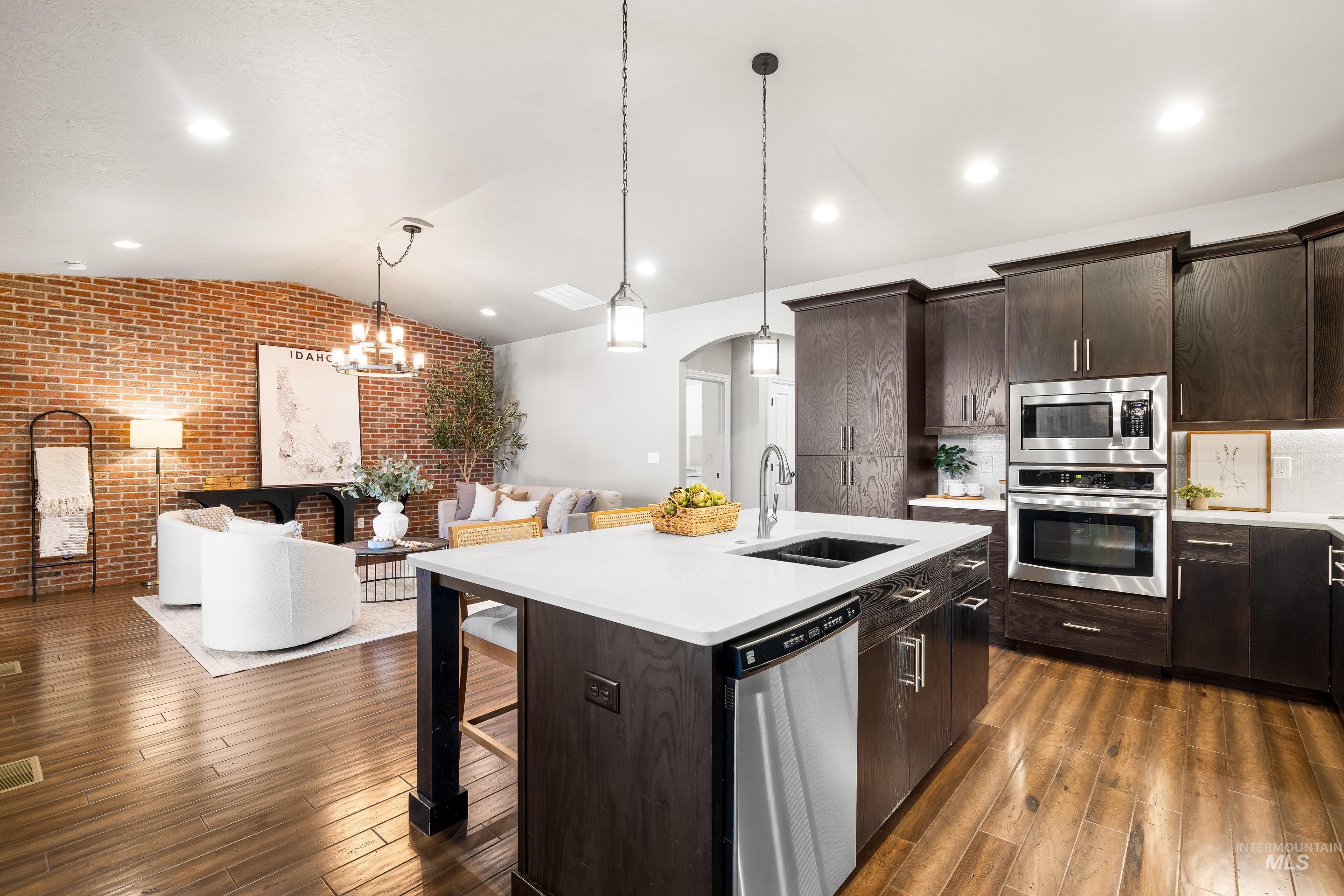Kitchen featuring brick wall, dark brown cabinets, vaulted ceiling, stainless steel appliances, and a kitchen breakfast bar