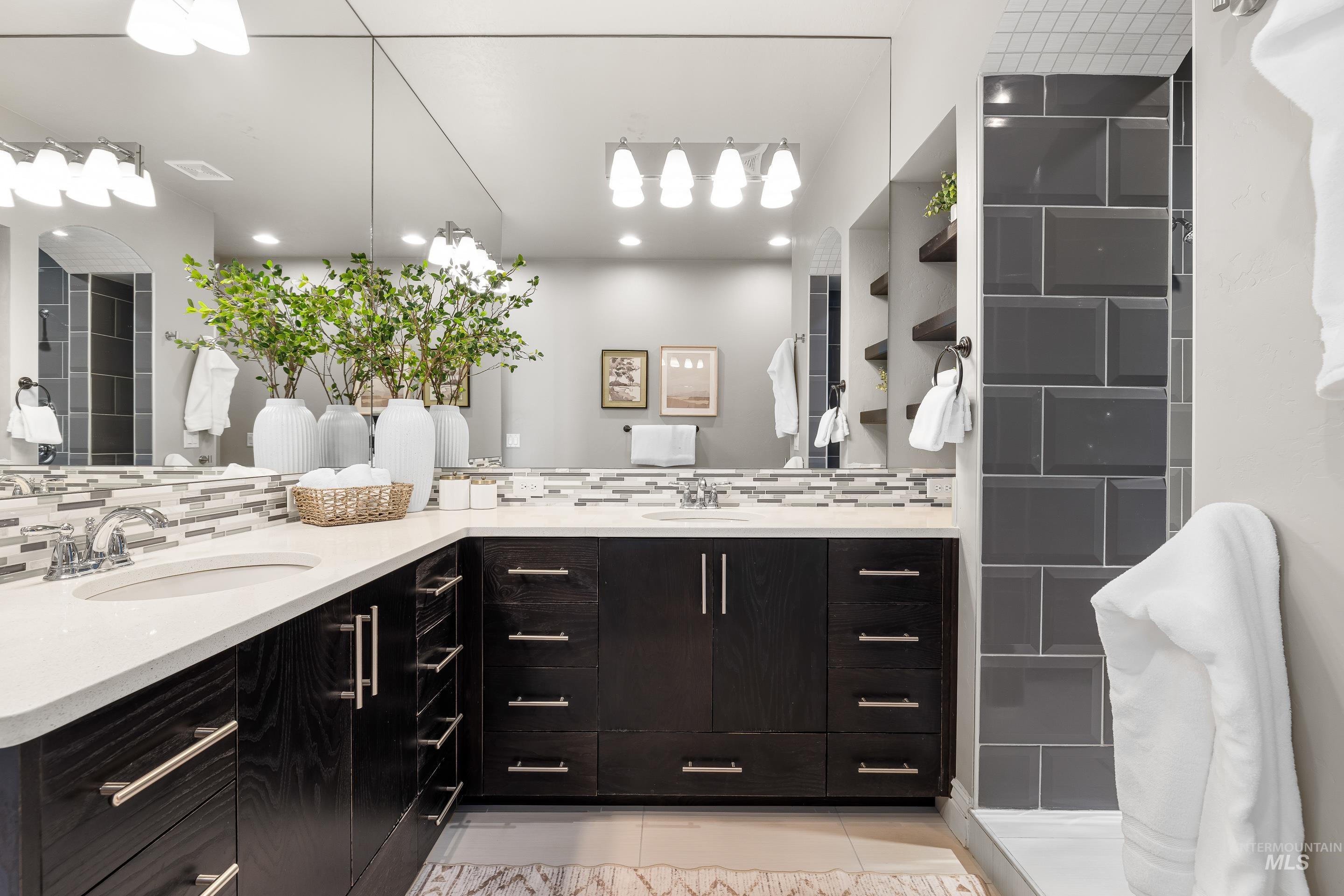 Full bath featuring double vanity, decorative backsplash, light tile patterned floors, and a walk in shower