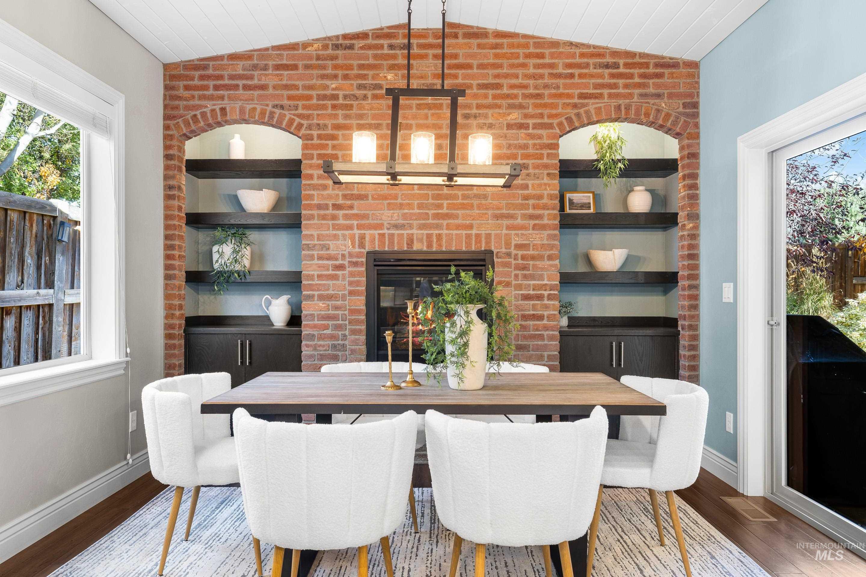 Dining area with healthy amount of natural light, lofted ceiling, built in features, wood finished floors, and brick wall