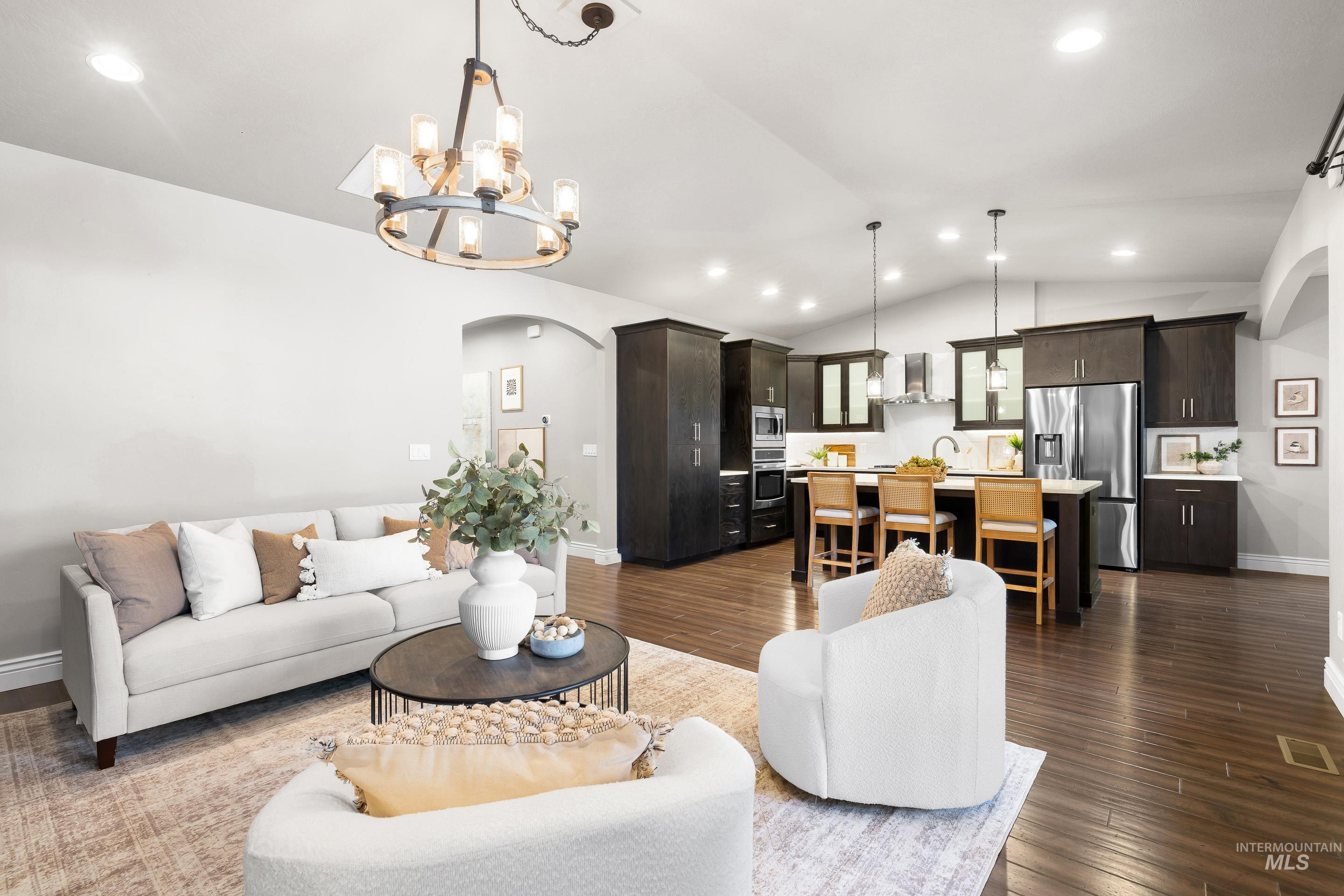 Living area with arched walkways, recessed lighting, dark wood finished floors, vaulted ceiling, and a chandelier