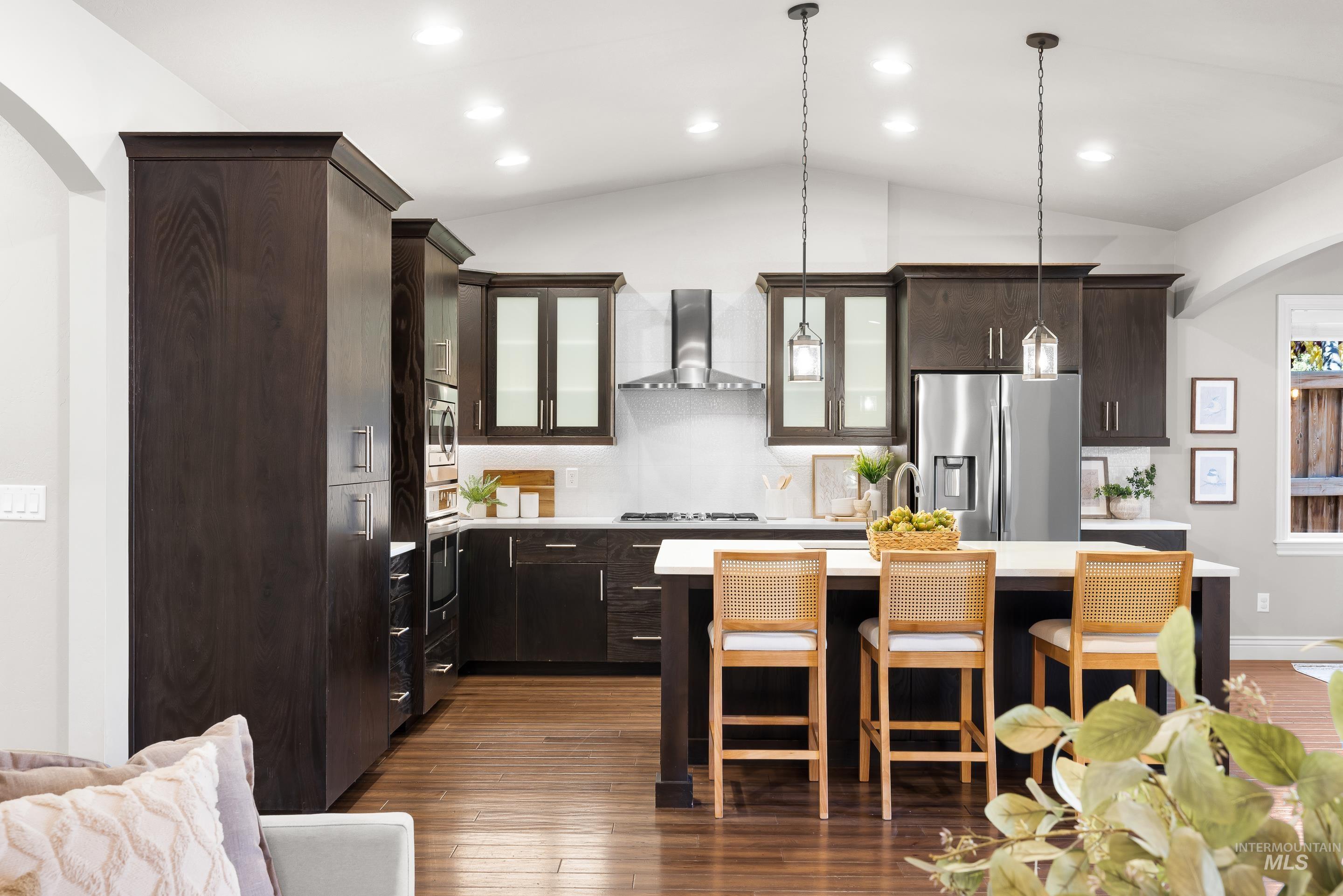 Kitchen with glass insert cabinets, vaulted ceiling, dark brown cabinets, a kitchen bar, and arched walkways