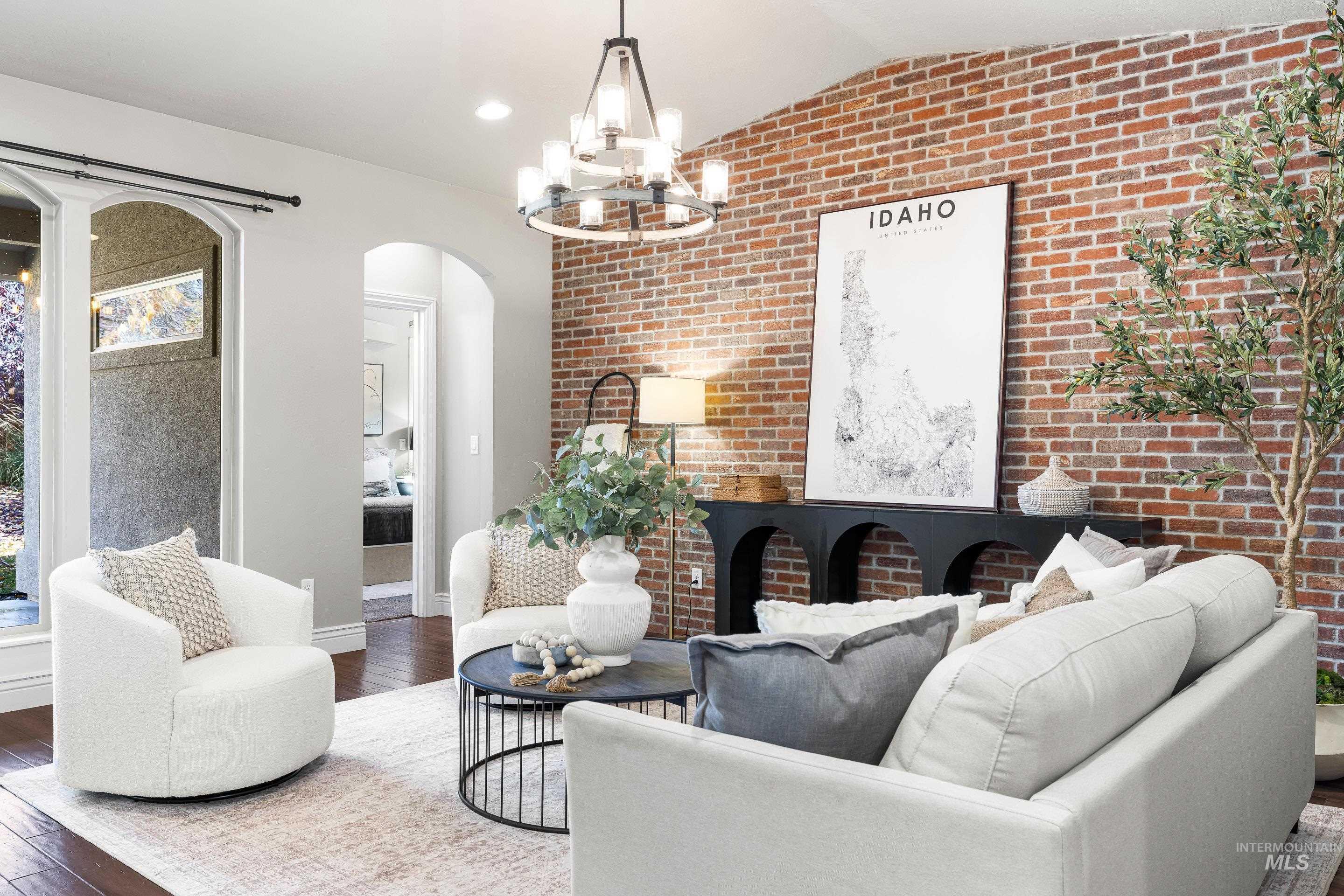 Living area with brick wall, wood-type flooring, arched walkways, a chandelier, and vaulted ceiling