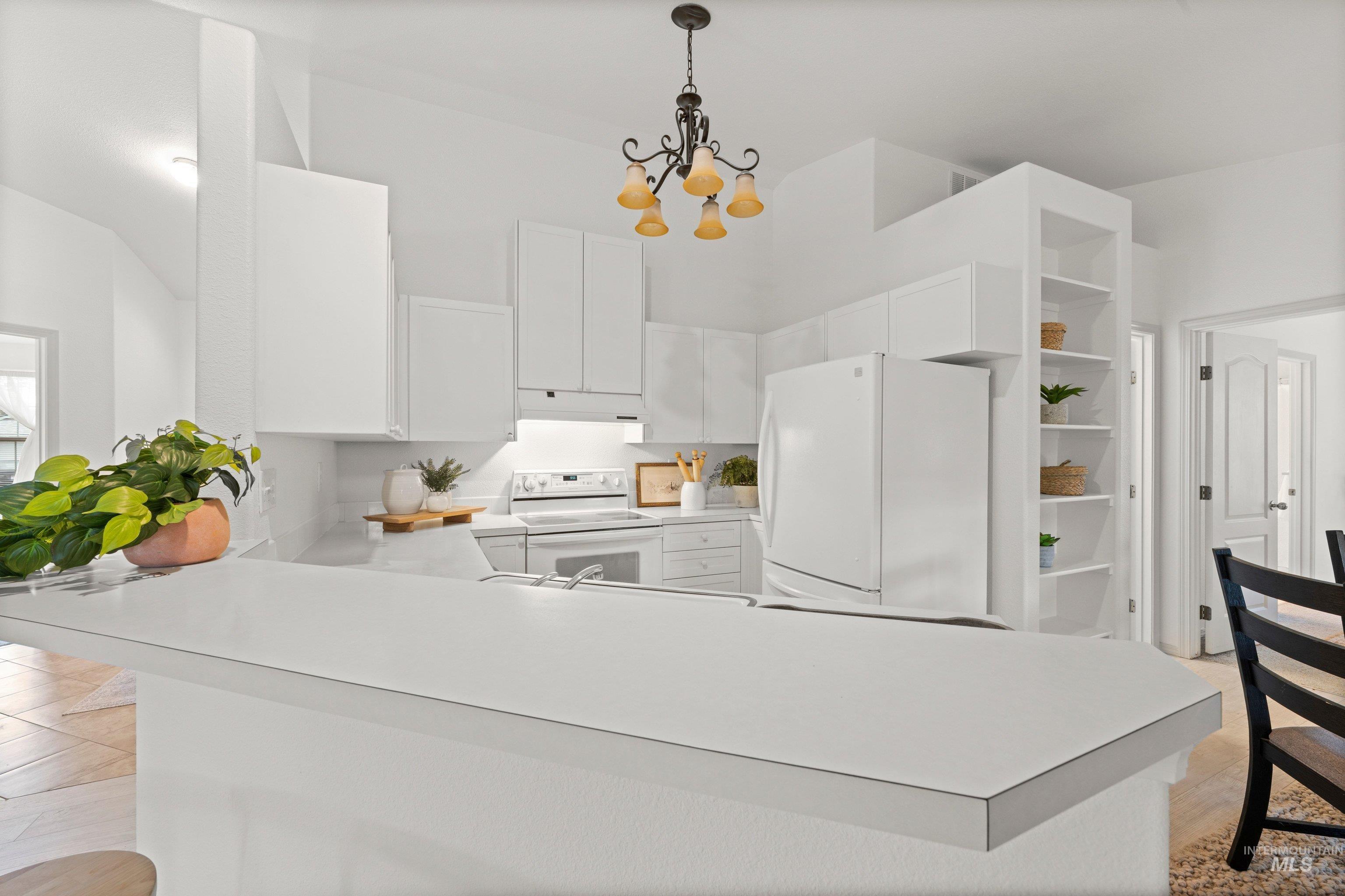 Kitchen with light countertops, white appliances, hanging lights, and white cabinetry