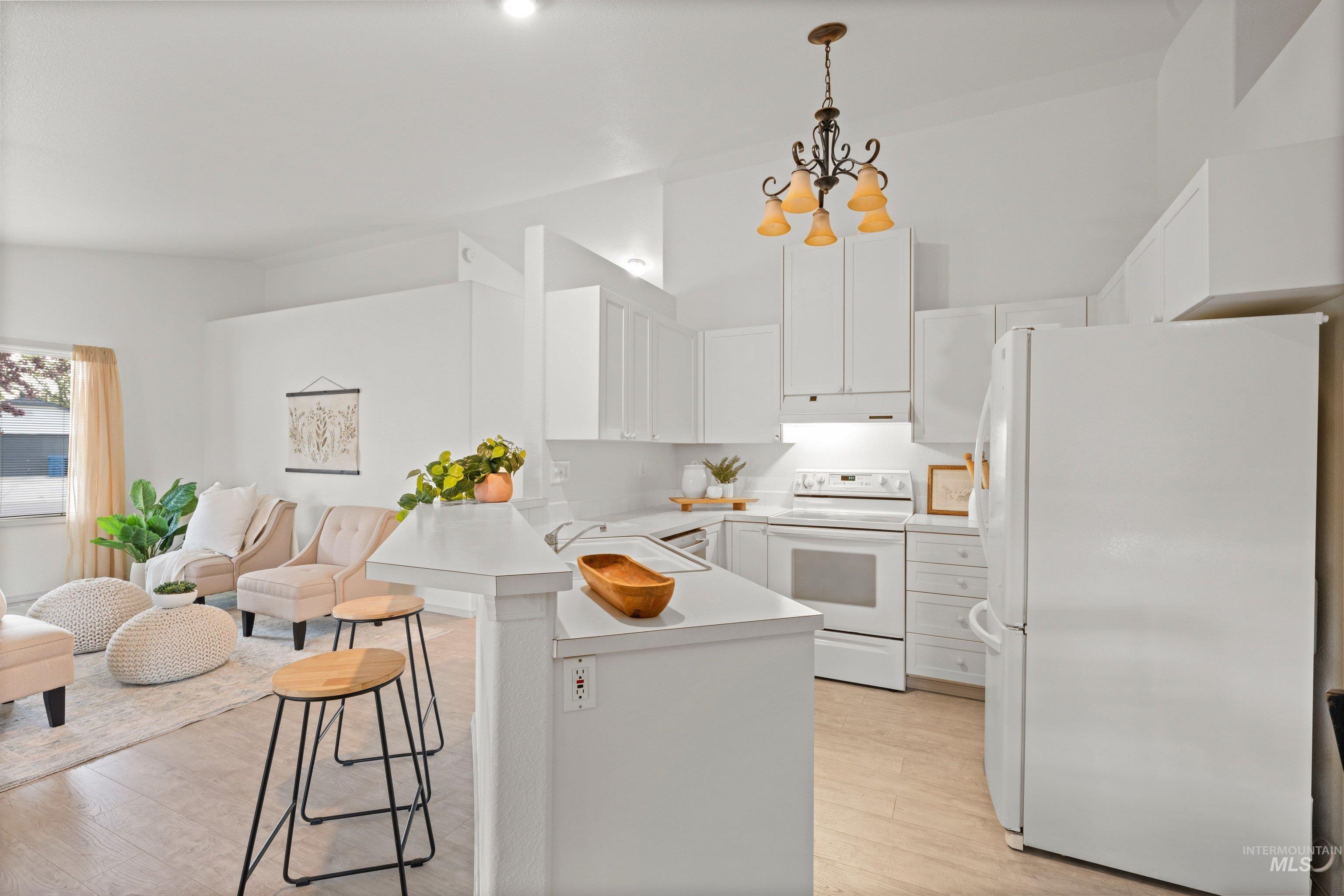 Kitchen featuring white appliances, light countertops, white cabinetry, a breakfast bar, and light wood-style flooring