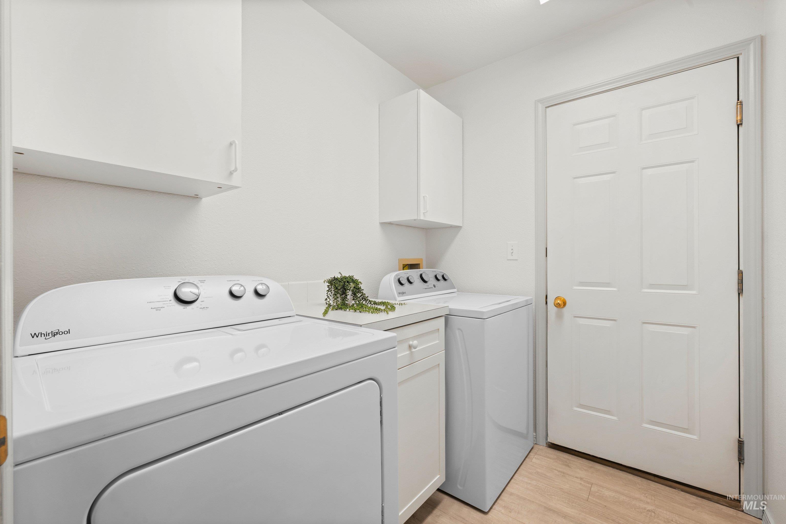 Laundry area featuring light wood-type flooring, washer and dryer, and cabinet space