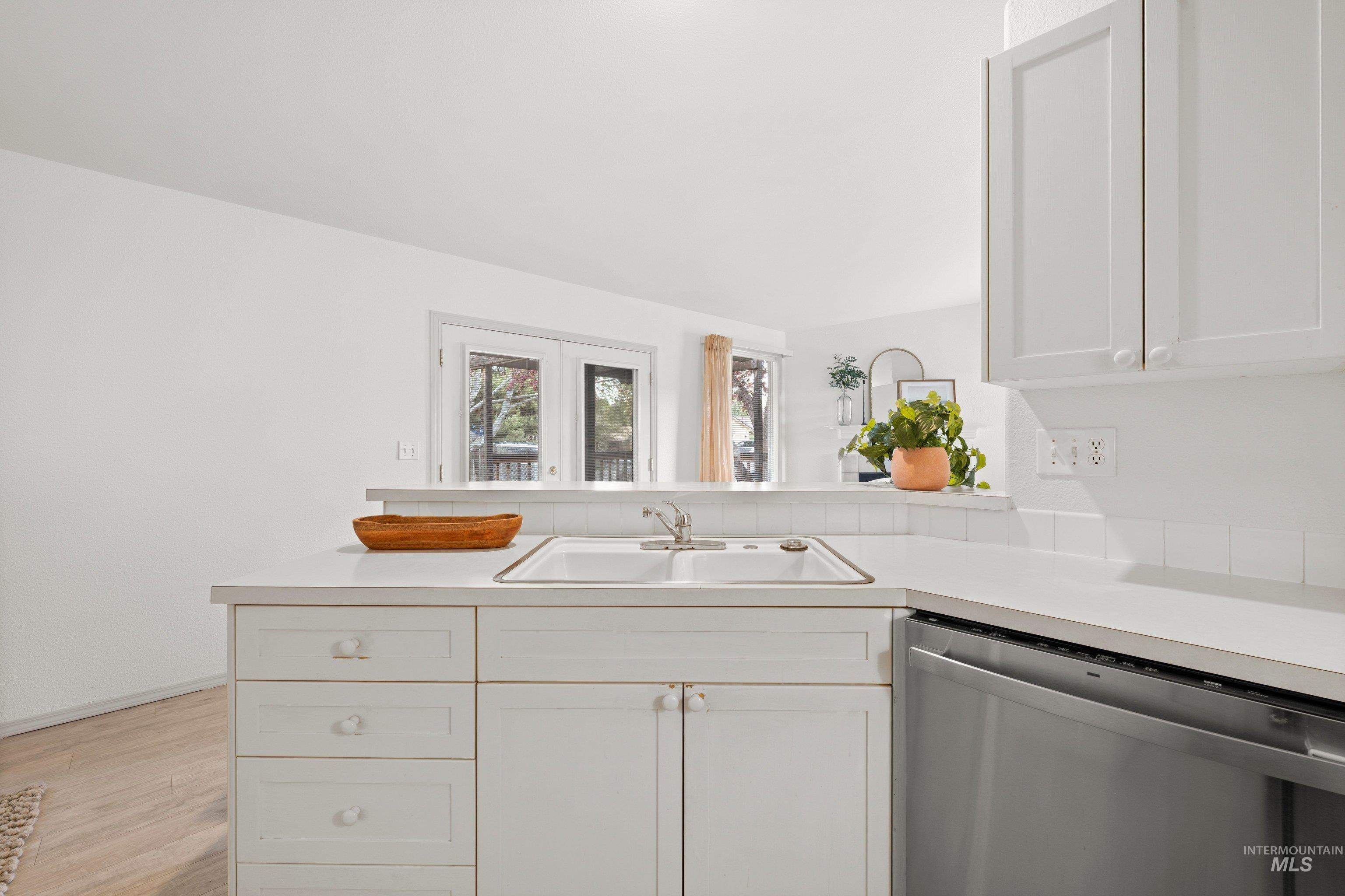 Kitchen featuring stainless steel dishwasher, light countertops, white cabinetry, a peninsula, and light wood finished floors