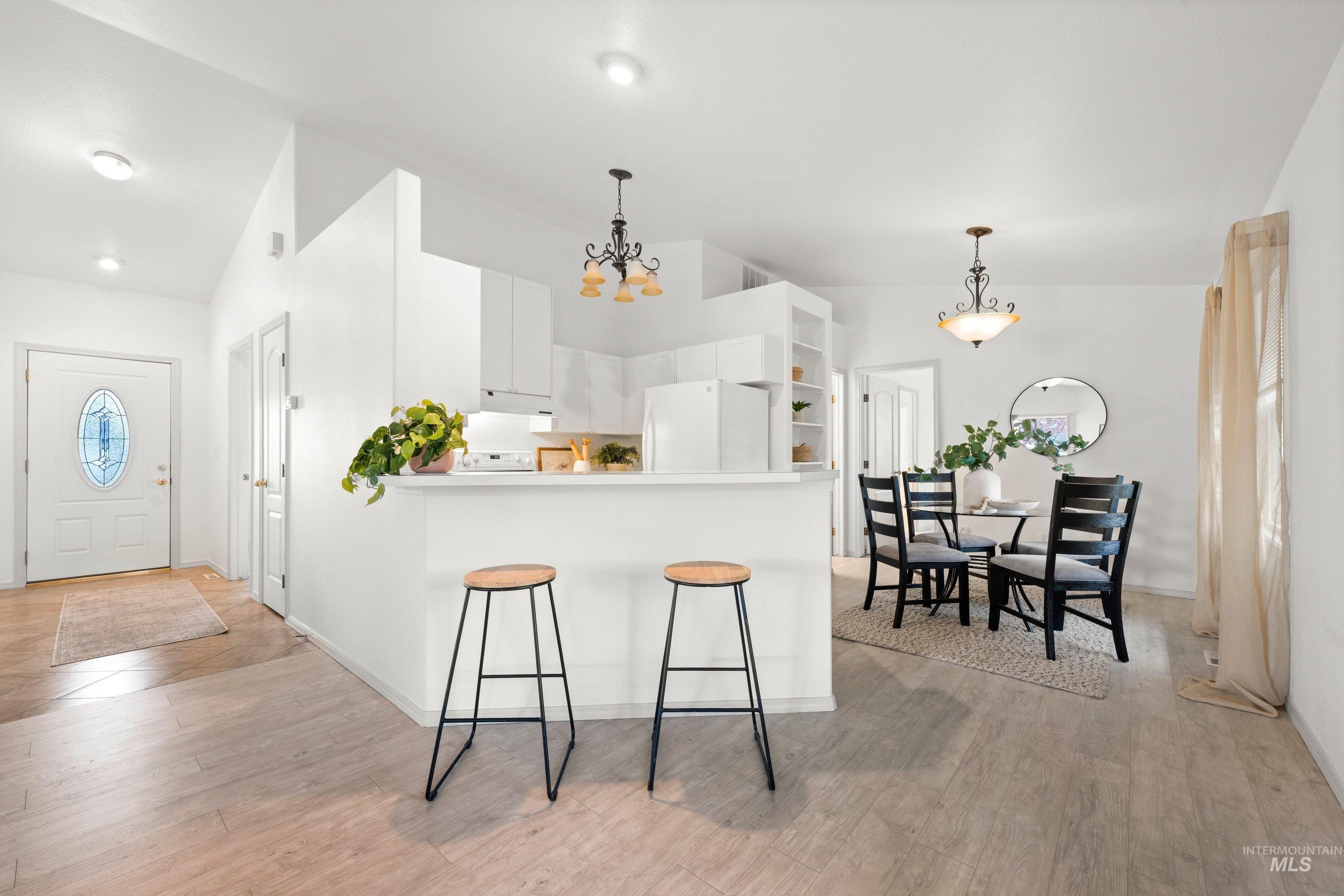 Kitchen with white cabinets, freestanding refrigerator, a peninsula, hanging lights, and light wood-style flooring