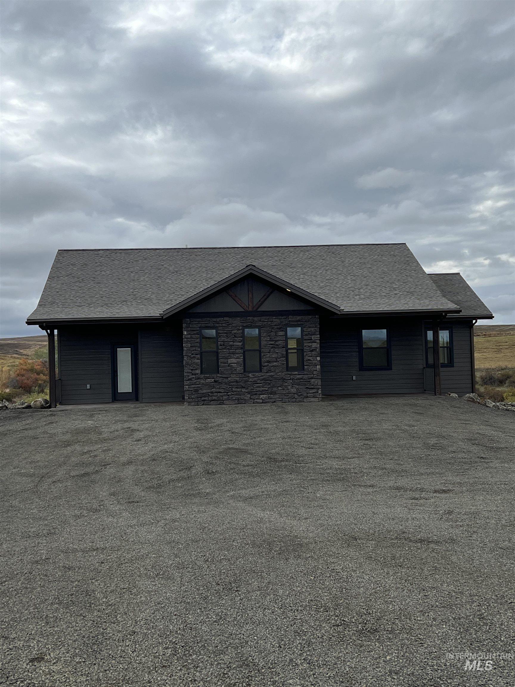 Ranch-style house featuring a shingled roof and stone siding
