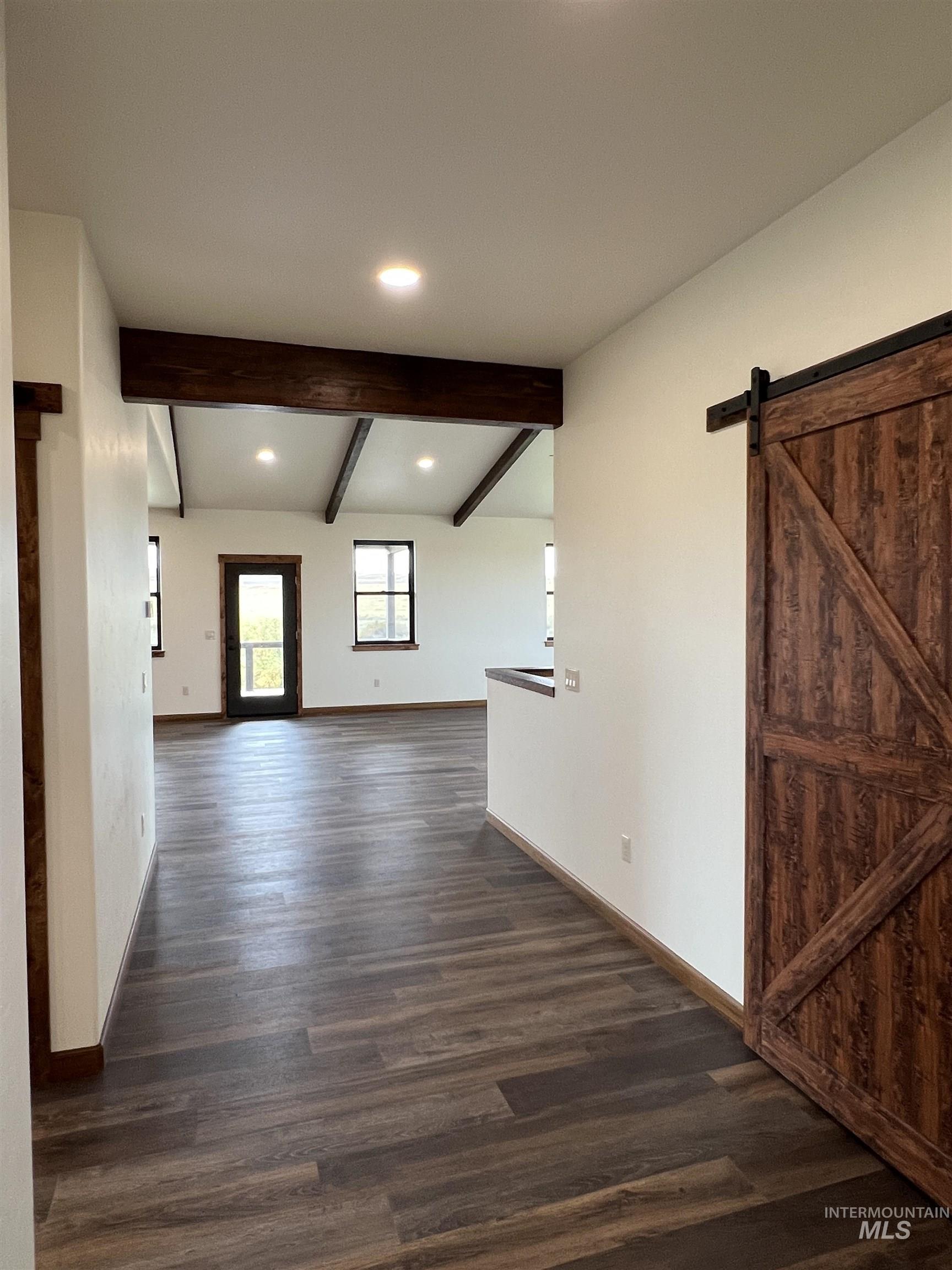 Unfurnished room featuring a barn door, beamed ceiling, dark wood-style flooring, and recessed lighting