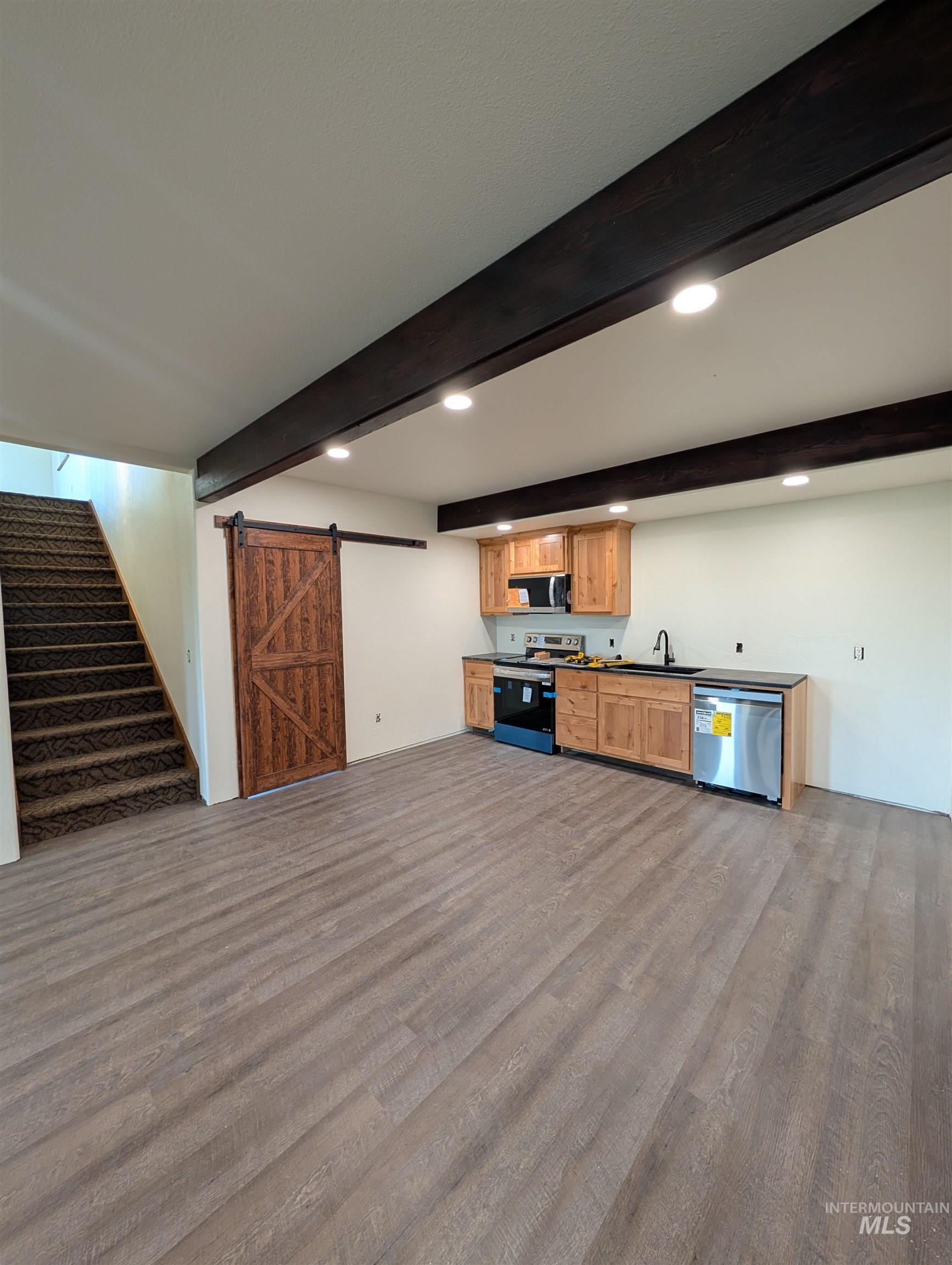 Kitchen featuring a barn door, beam ceiling, stainless steel appliances, recessed lighting, and dark countertops