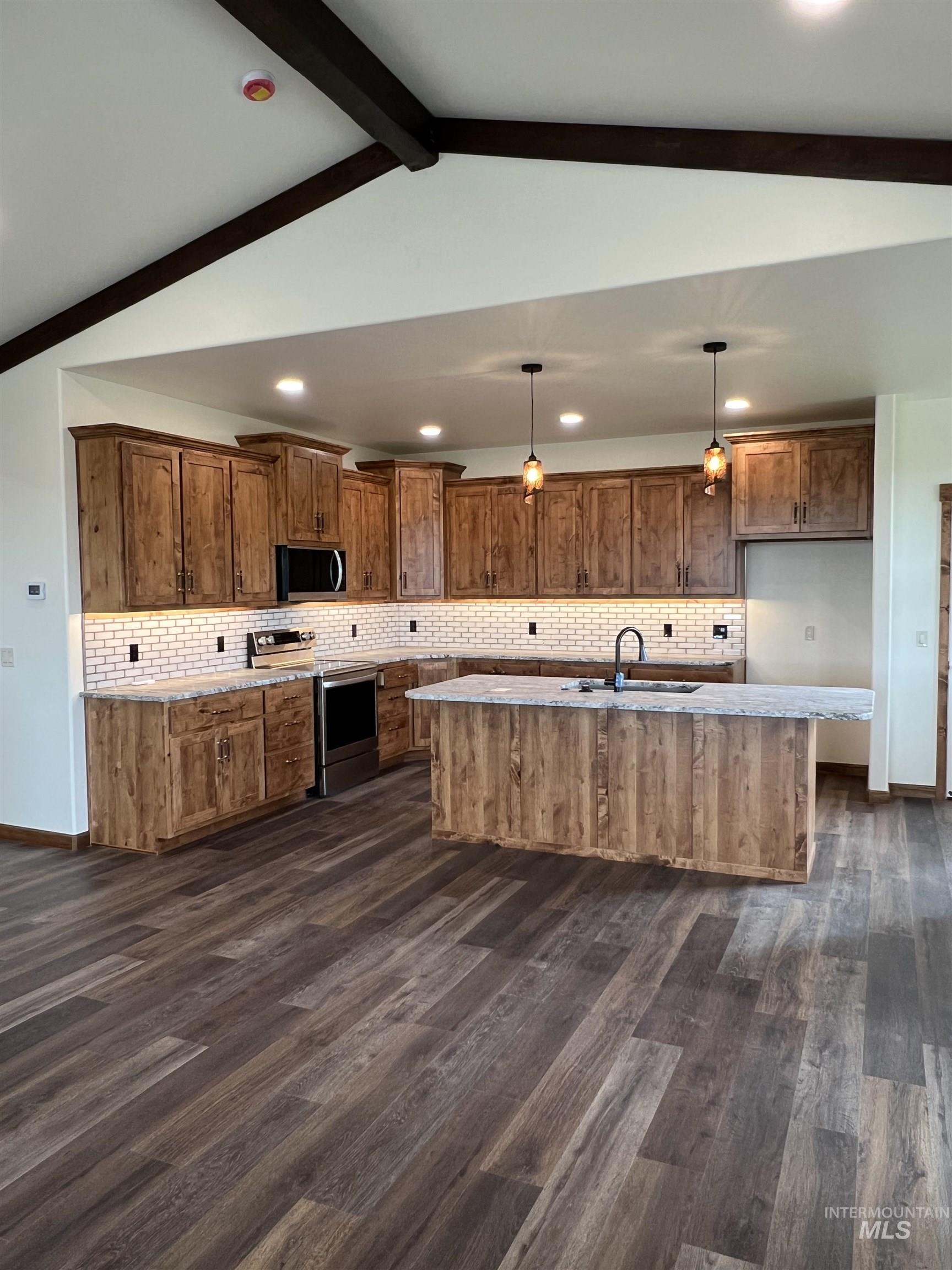 Kitchen featuring brown cabinets, appliances with stainless steel finishes, hanging light fixtures, dark wood-type flooring, and recessed lighting