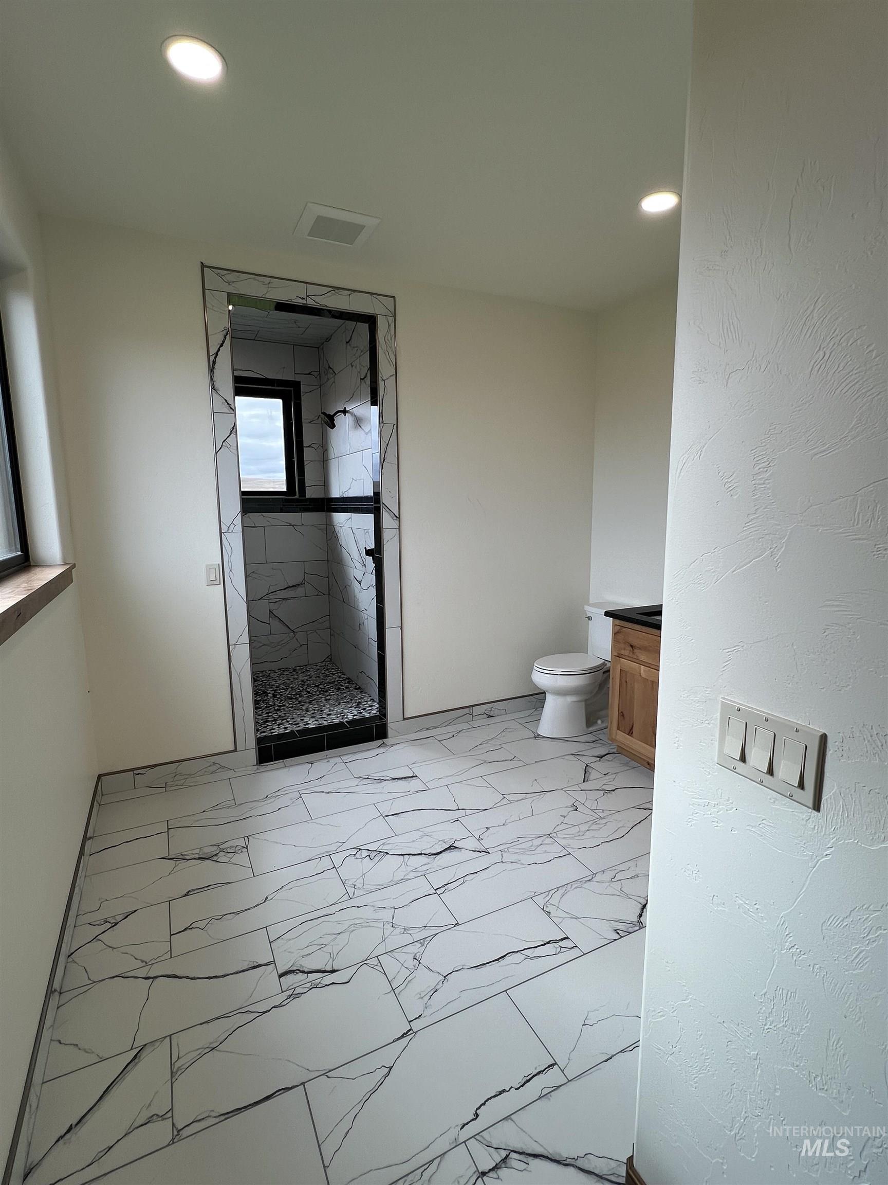 Bathroom featuring vanity, light marble finish flooring, a marble finish shower, and recessed lighting